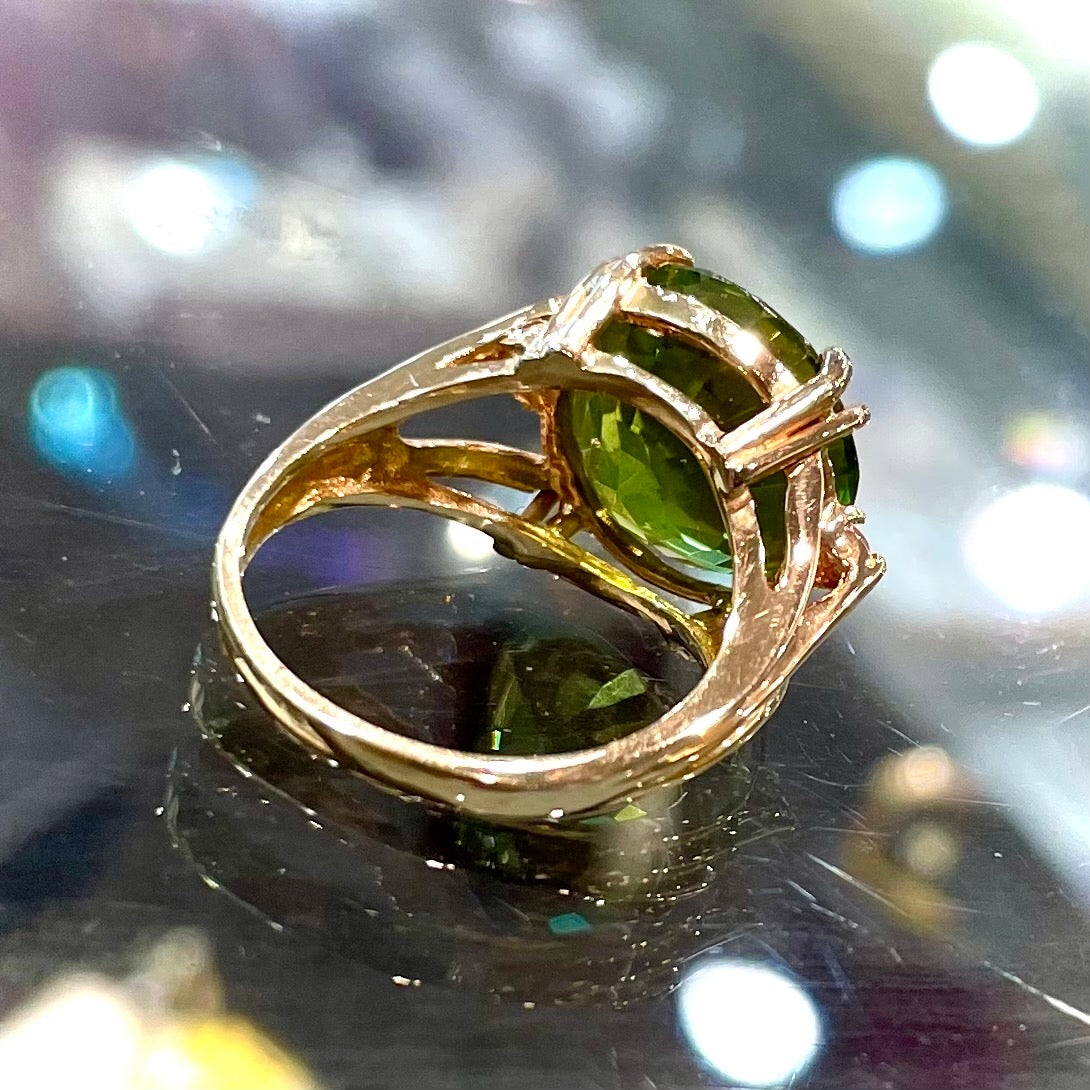 A ladies' round brilliant cut peridot statement ring set with two round diamond accents in yellow gold.