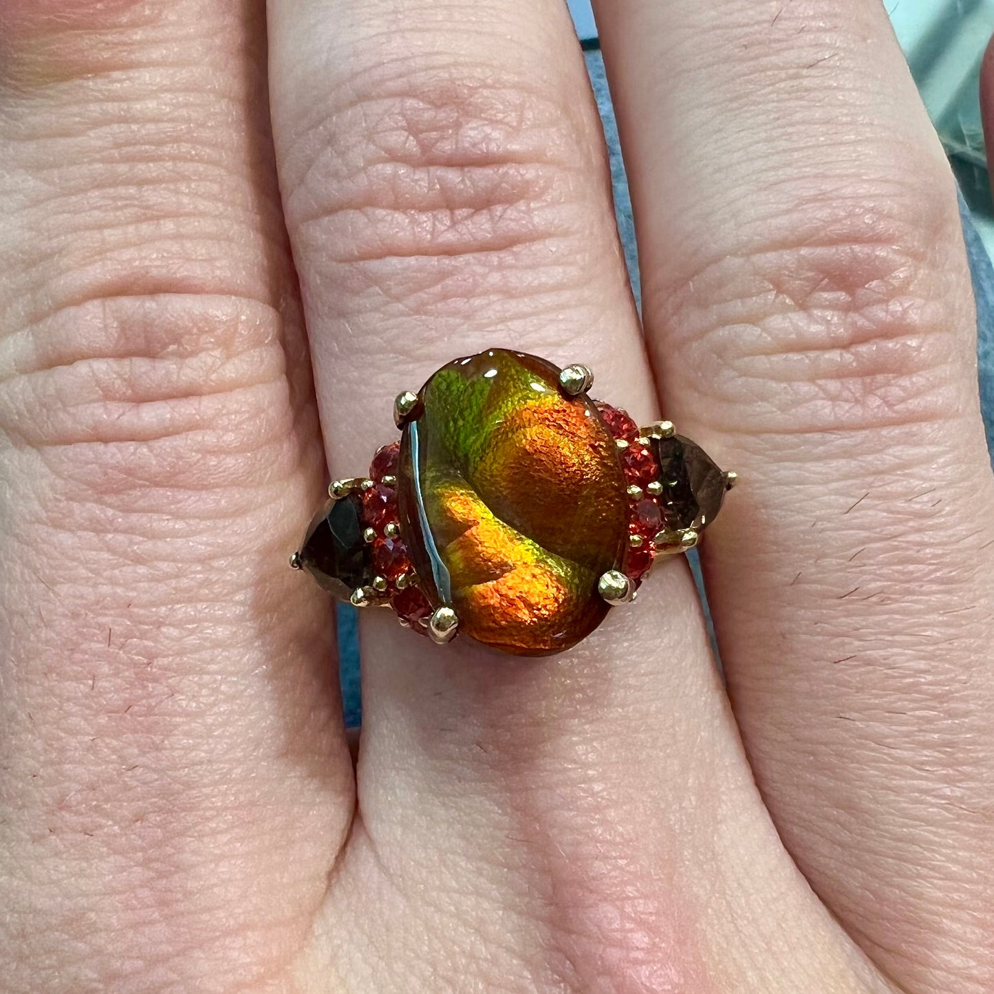 A ladies yellow gold fire agate ring set with trillion cut smoky quartz and round cut red-orange garnet accents. The fire agate displays green and red.