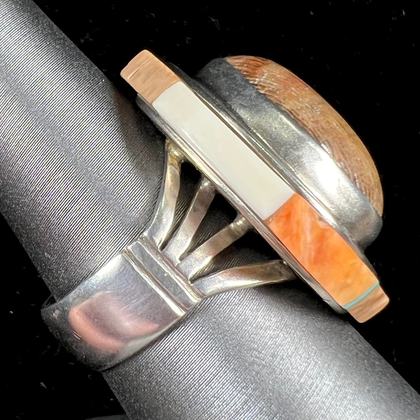 A silver ring handmade from a bezel set petrified wood stone, surrounded by quartz, carnelian, and bone inlay.