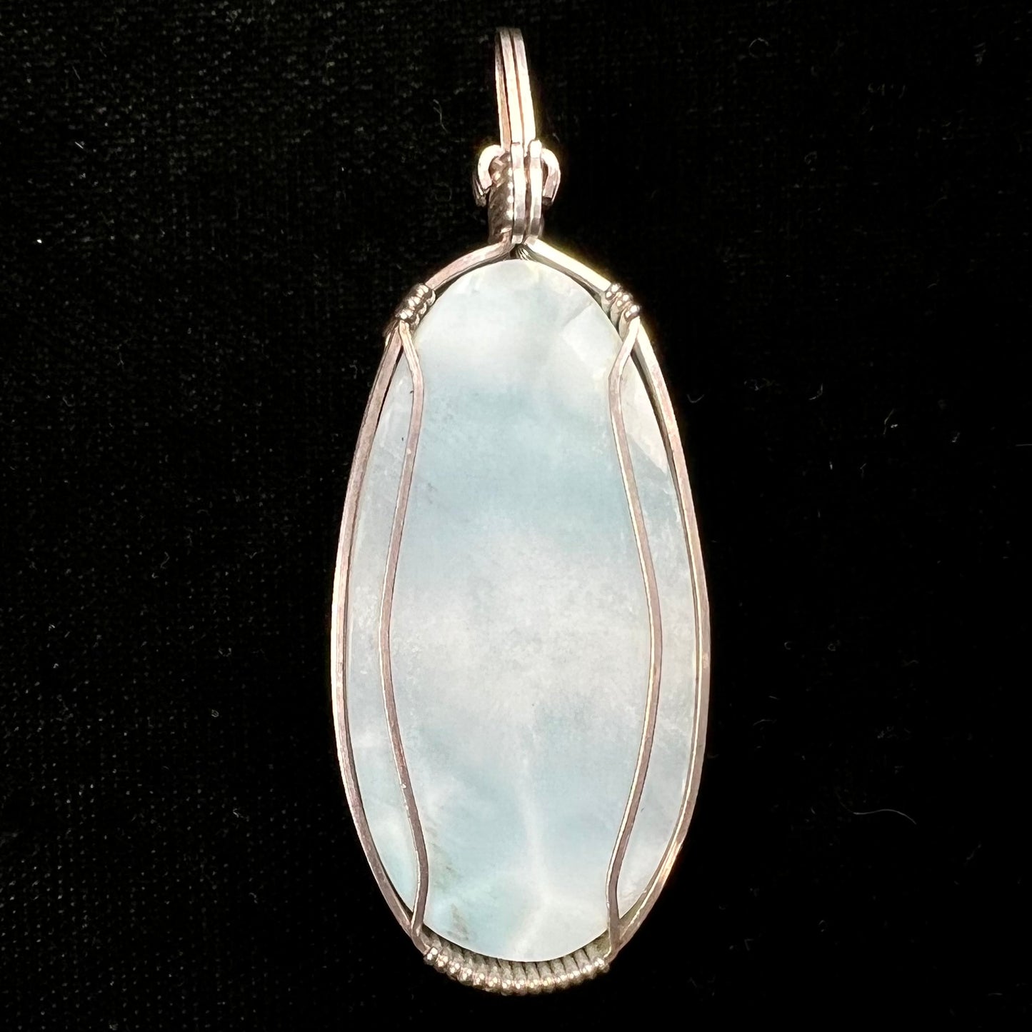 A large, oval cabochon cut blue larimar stone mounted in a sterling silver wire wrapped pendant.