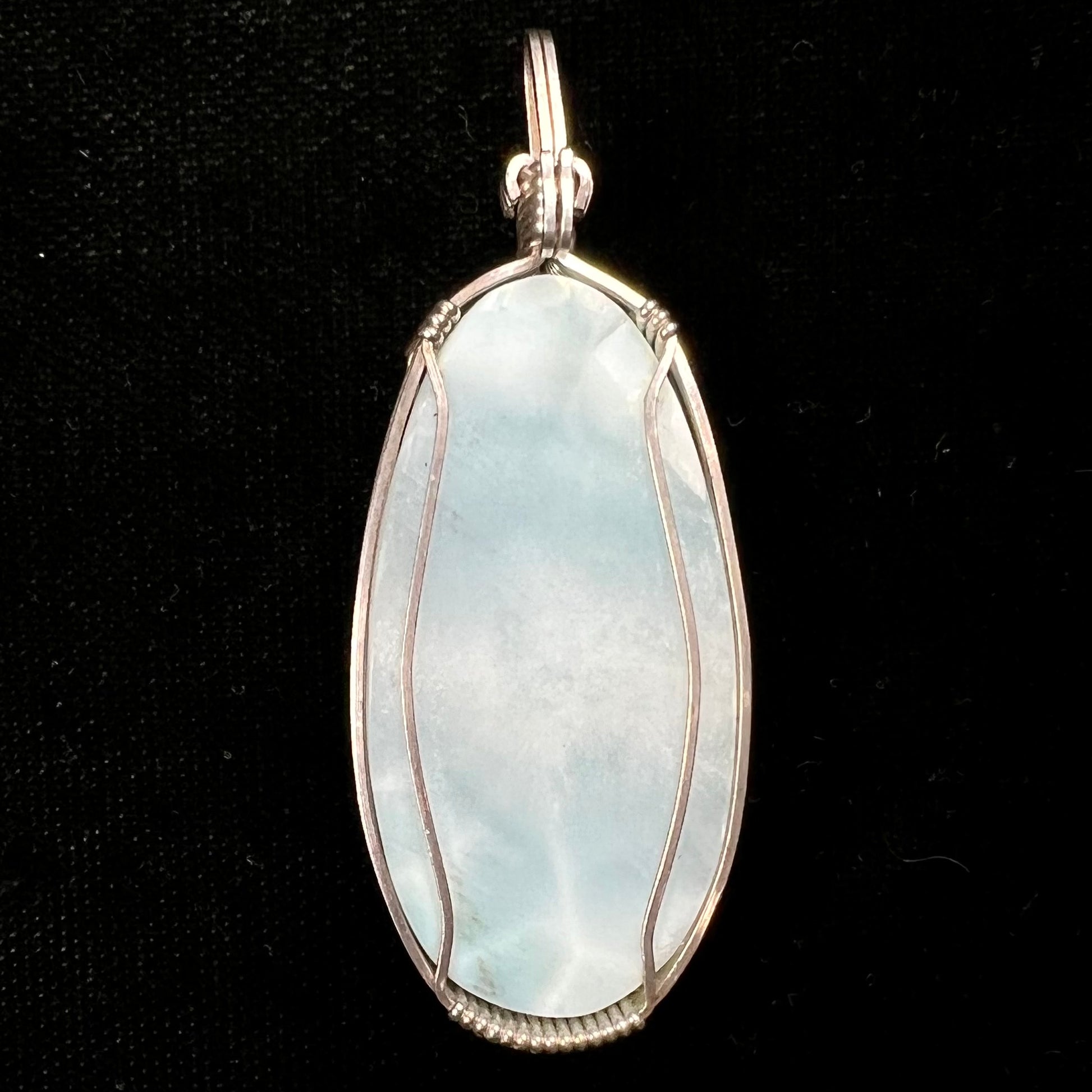 A large, oval cabochon cut blue larimar stone mounted in a sterling silver wire wrapped pendant.