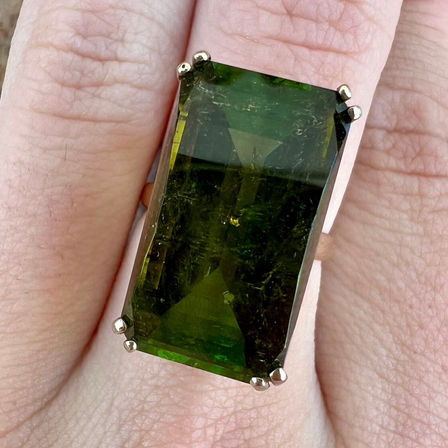 A faceted step-cut dark green tourmaline basket set solitaire ring cast in yellow gold.