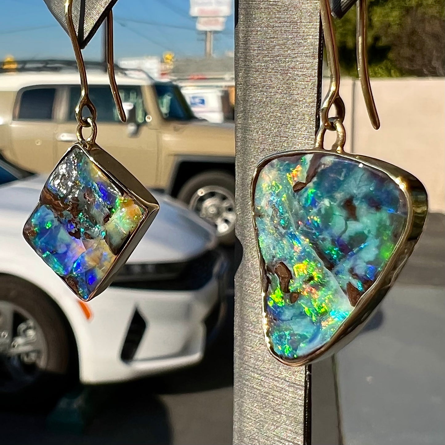 An asymmetric pair of French wire dangle yellow gold boulder opal earrings. One opal is a square, and the other is a triangle.