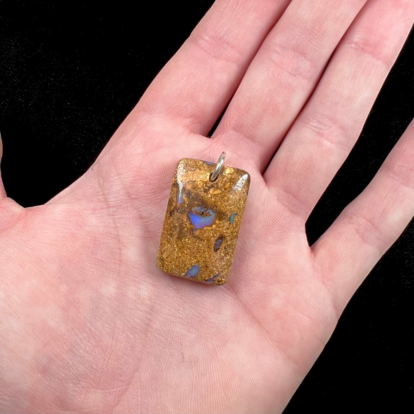 A drilled boulder opal stone with a sterling silver ring through the hole to be worn as a pendant.