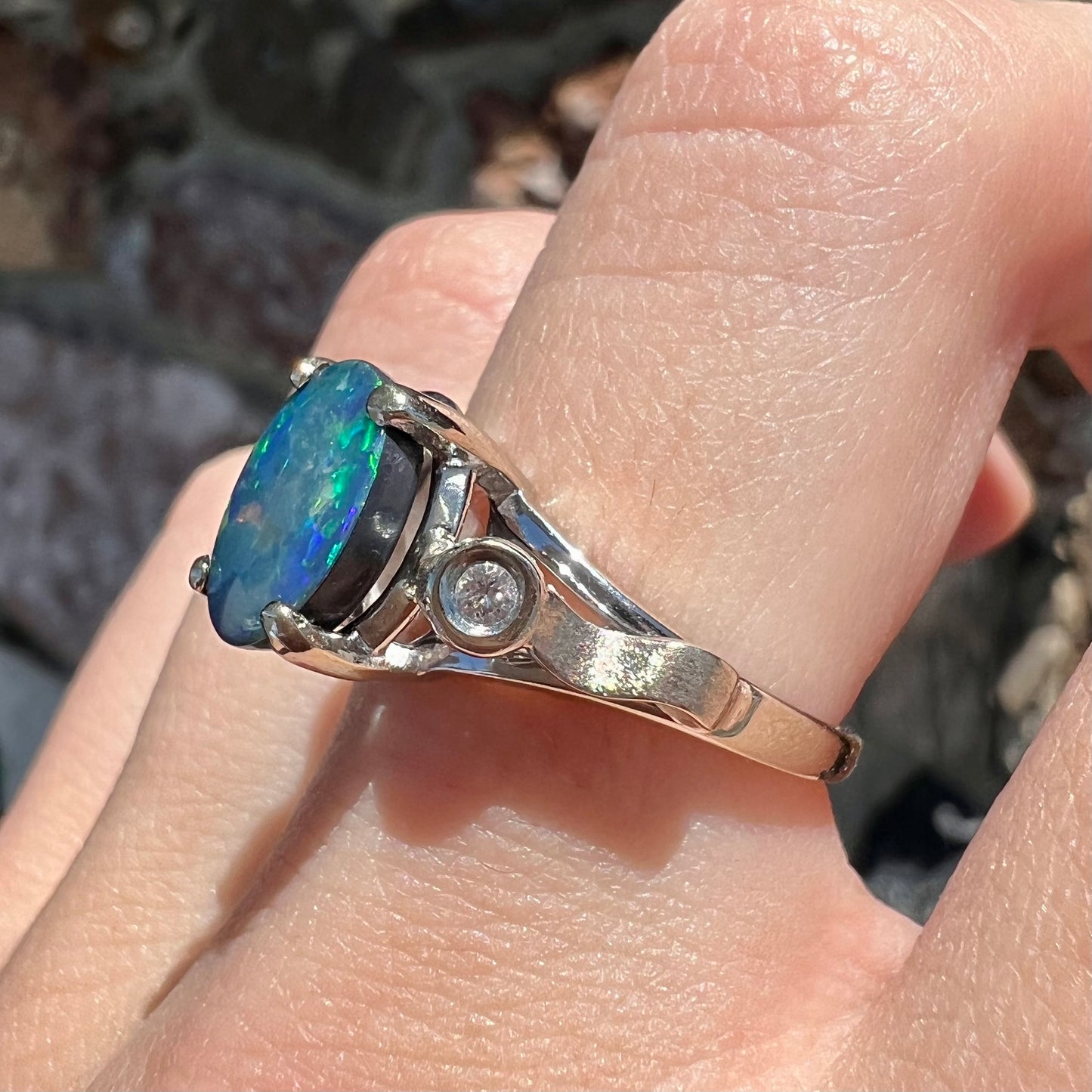 A white gold, oval cabochon cut black opal doublet ring set with two round diamond accent stones.