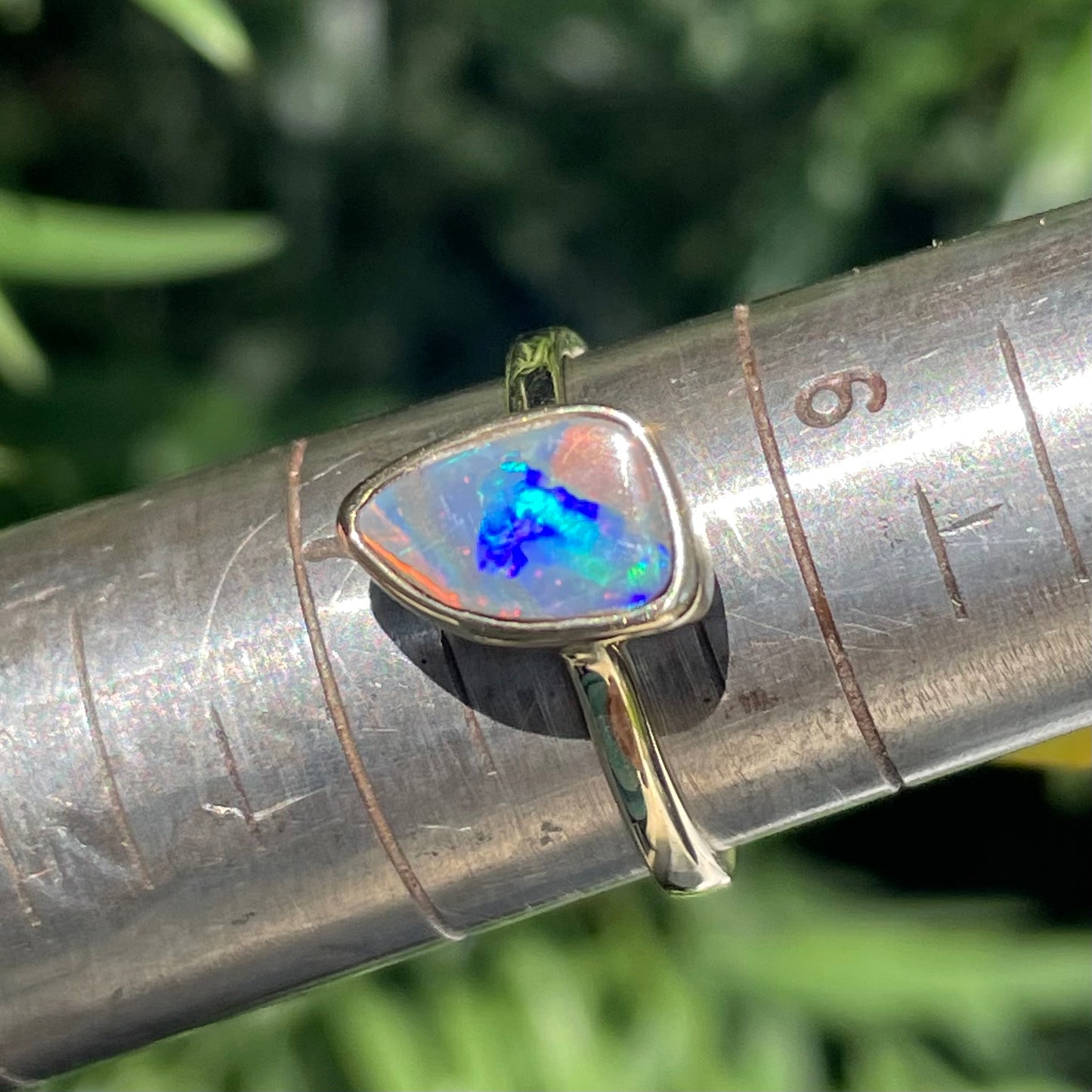 A handmade yellow gold solitaire ring bezel set with a Lightning Ridge red-on-black harlequin opal.