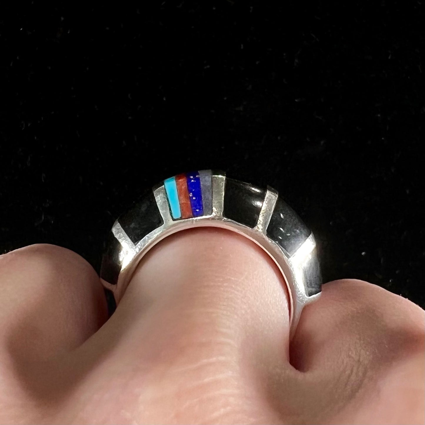 A sterling silver ring inlaid with onyx, turquoise, coral, lapis lazuli, and mother of pearl stones.