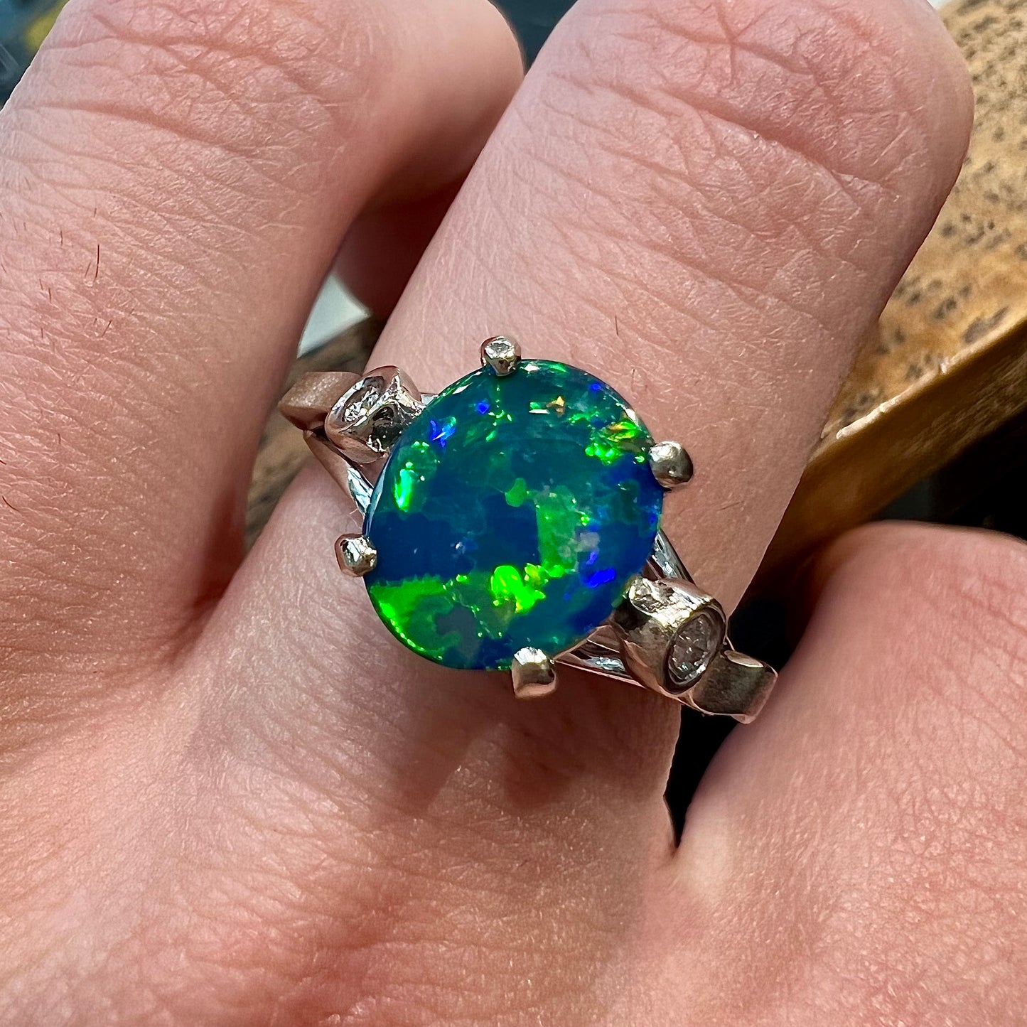 A white gold, oval cabochon cut black opal doublet ring set with two round diamond accent stones.