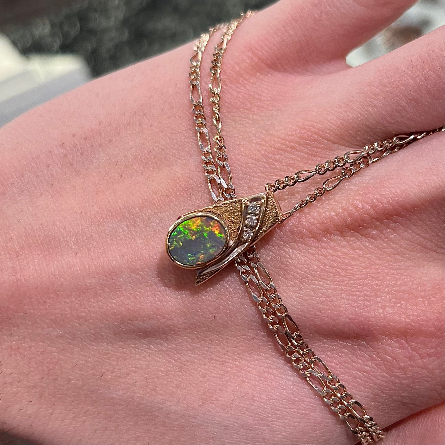 A yellow gold black opal necklace set with three round diamond accents.