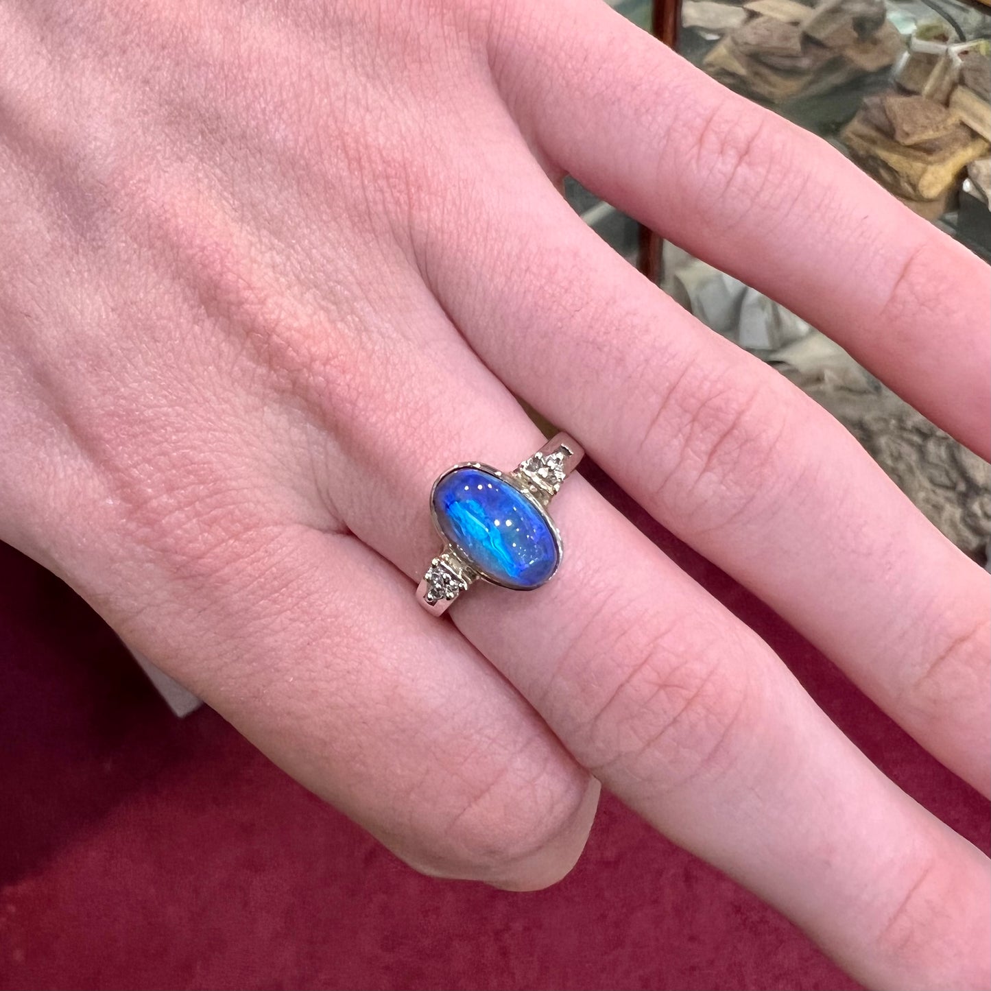 A white gold ring set with a Lightning Ridge black opal and diamond accents. The opal displays a cat's eye pattern.