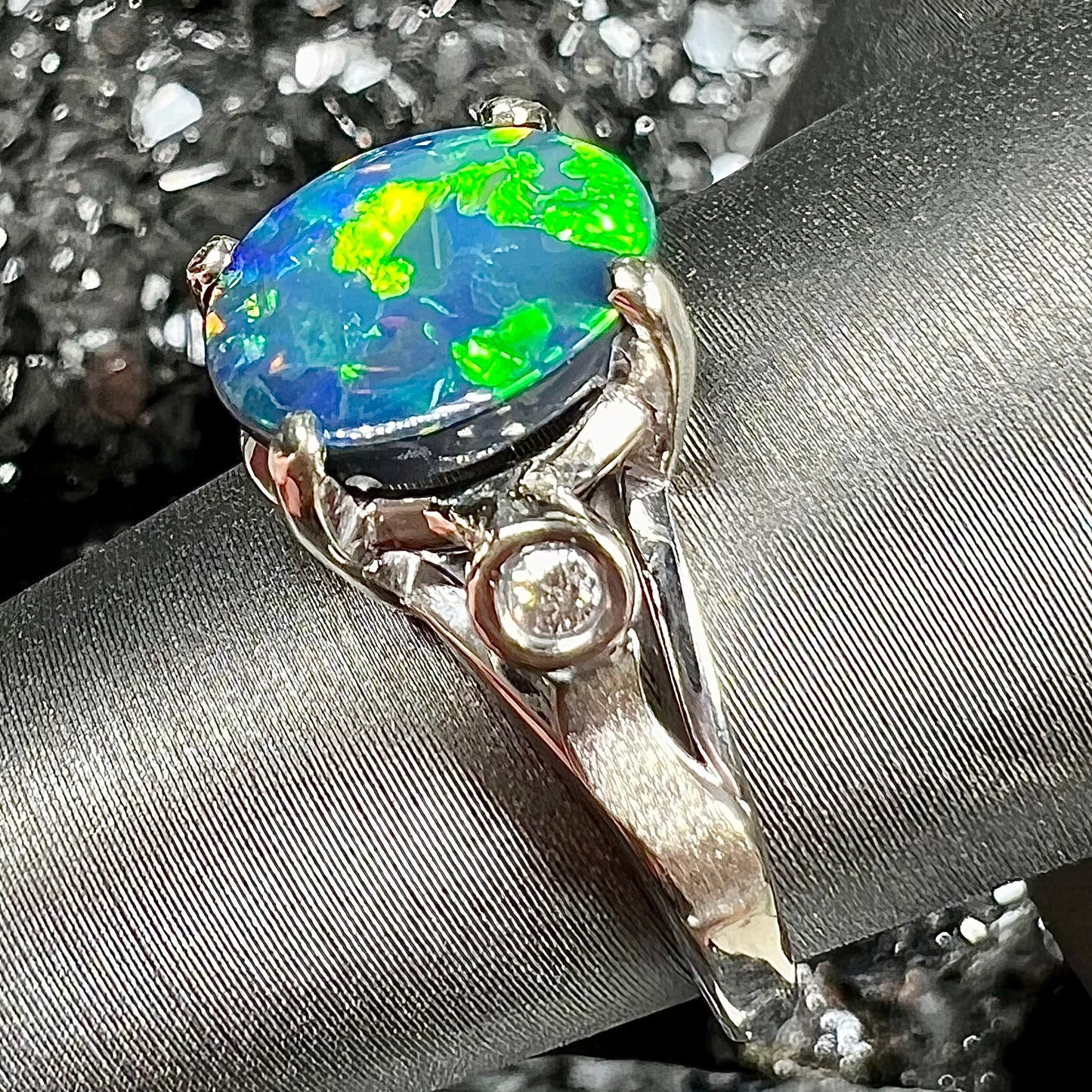 A white gold, oval cabochon cut black opal doublet ring set with two round diamond accent stones.