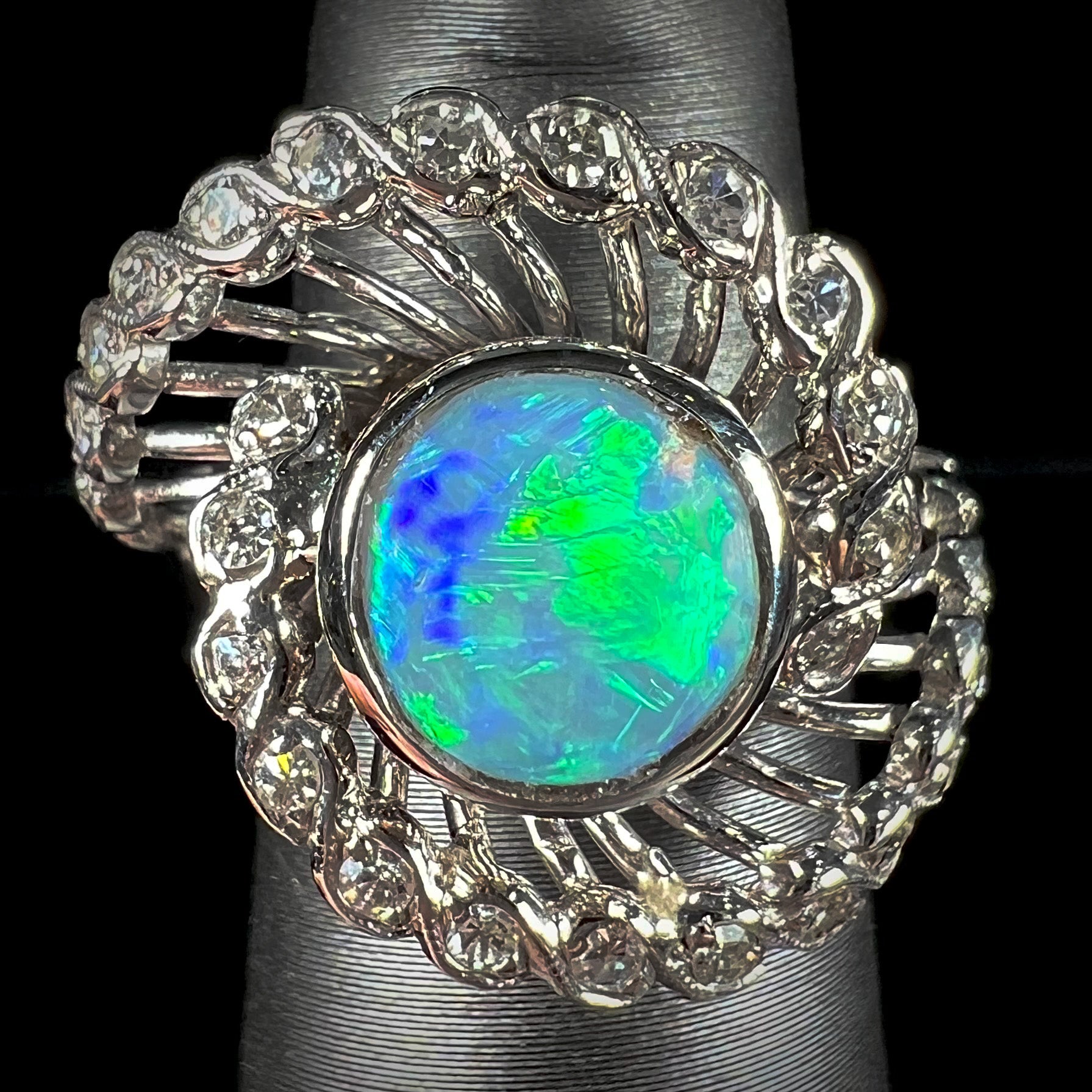 A white gold ring featuring a round cabochon cut black opal set in a swirl of round cut diamonds.