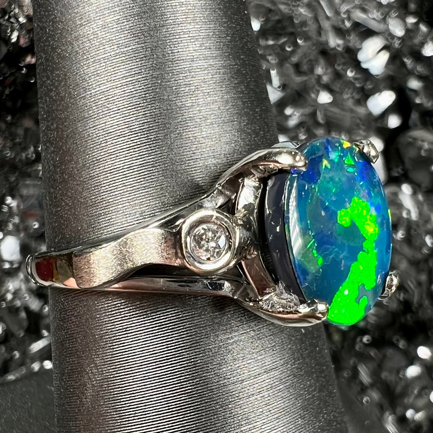 A white gold, oval cabochon cut black opal doublet ring set with two round diamond accent stones.