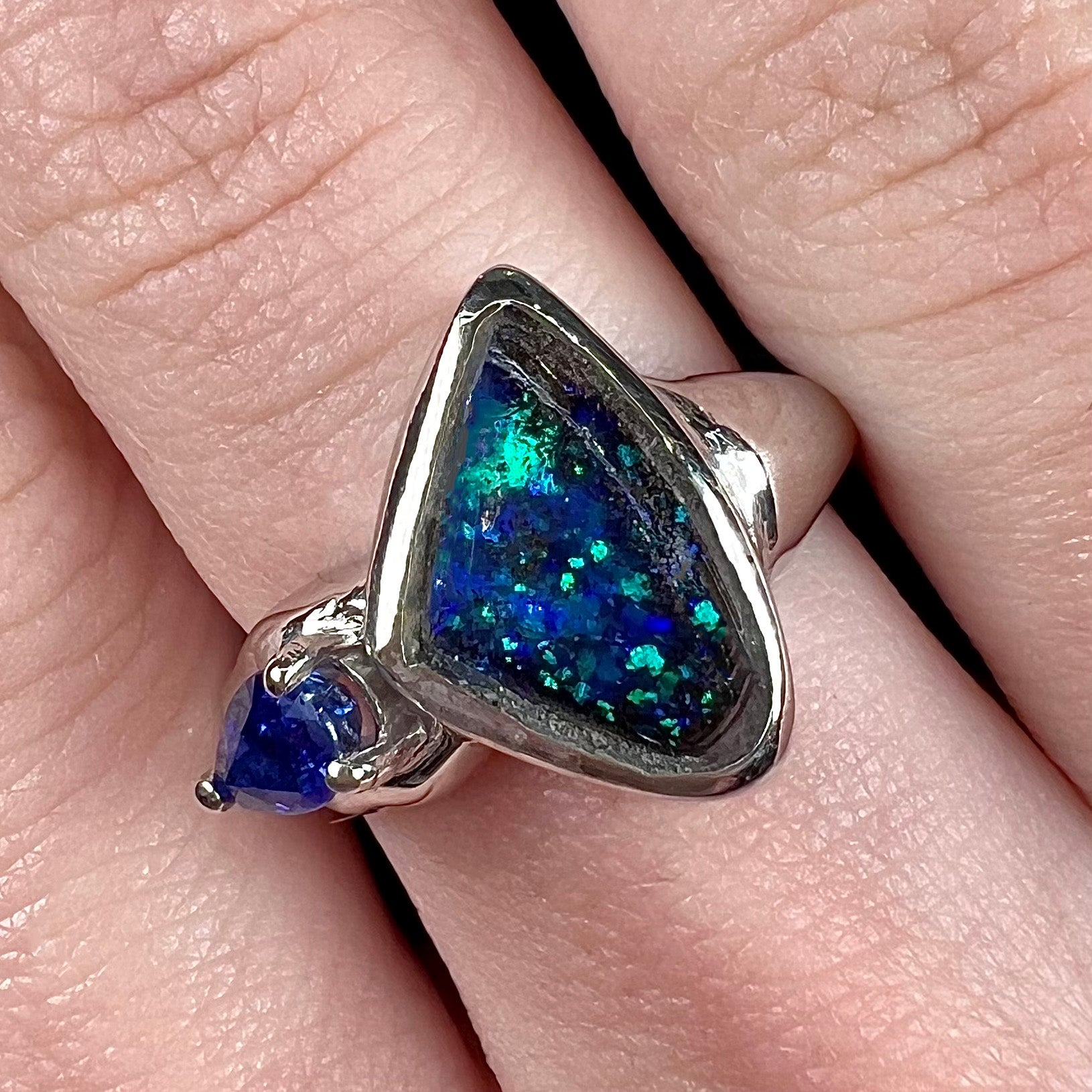 A ladies' white gold ring set with Australian black boulder opal and pear shape blue sapphire.