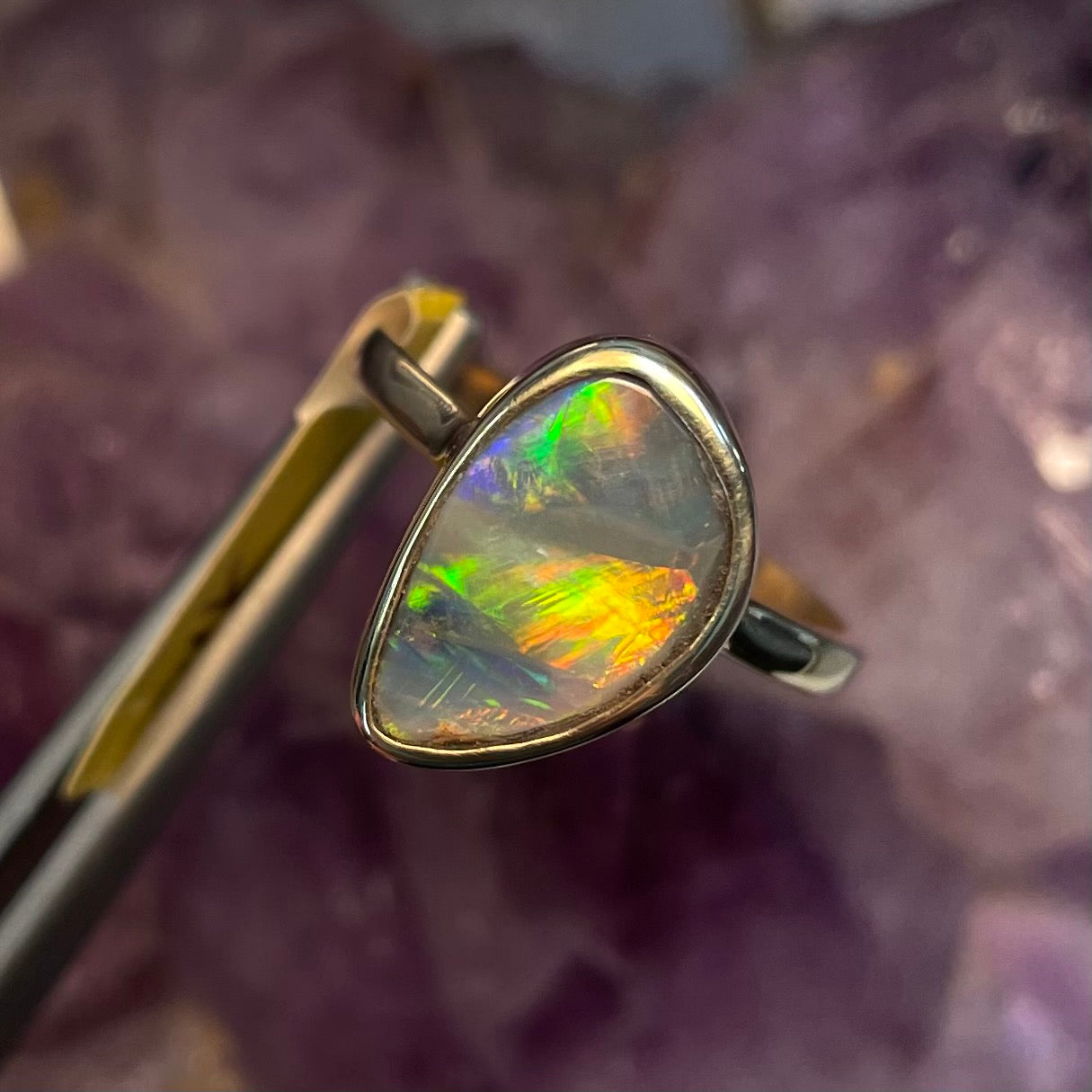 A freeform cut semi-black opal from Lightning Ridge, Australia set in a bezel set yellow gold solitaire ring.