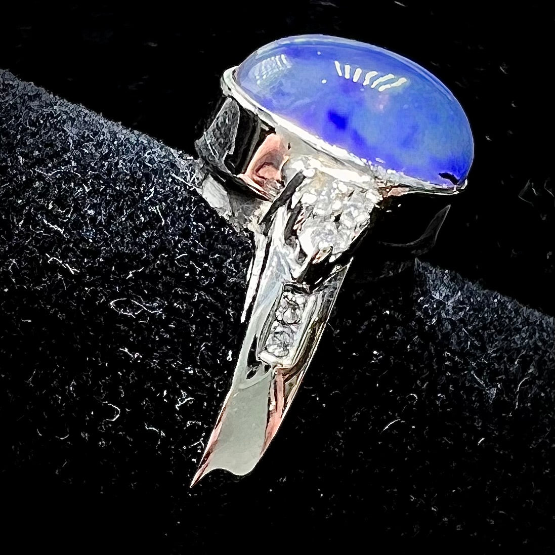 A white gold ring set with a Lightning Ridge black opal and diamond accents. The opal displays a cat's eye pattern.