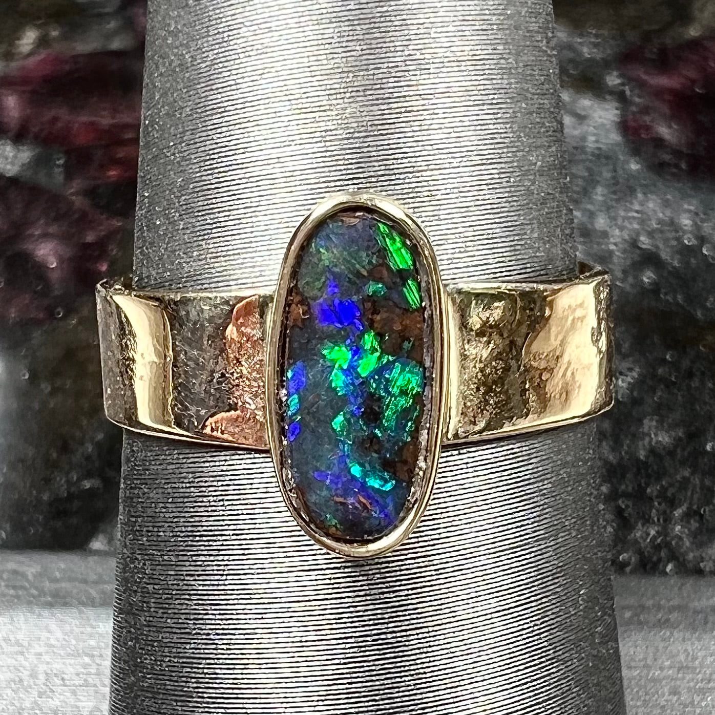 A blue green oval cabochon cut Australian boulder opal set in a yellow gold solitaire ring.