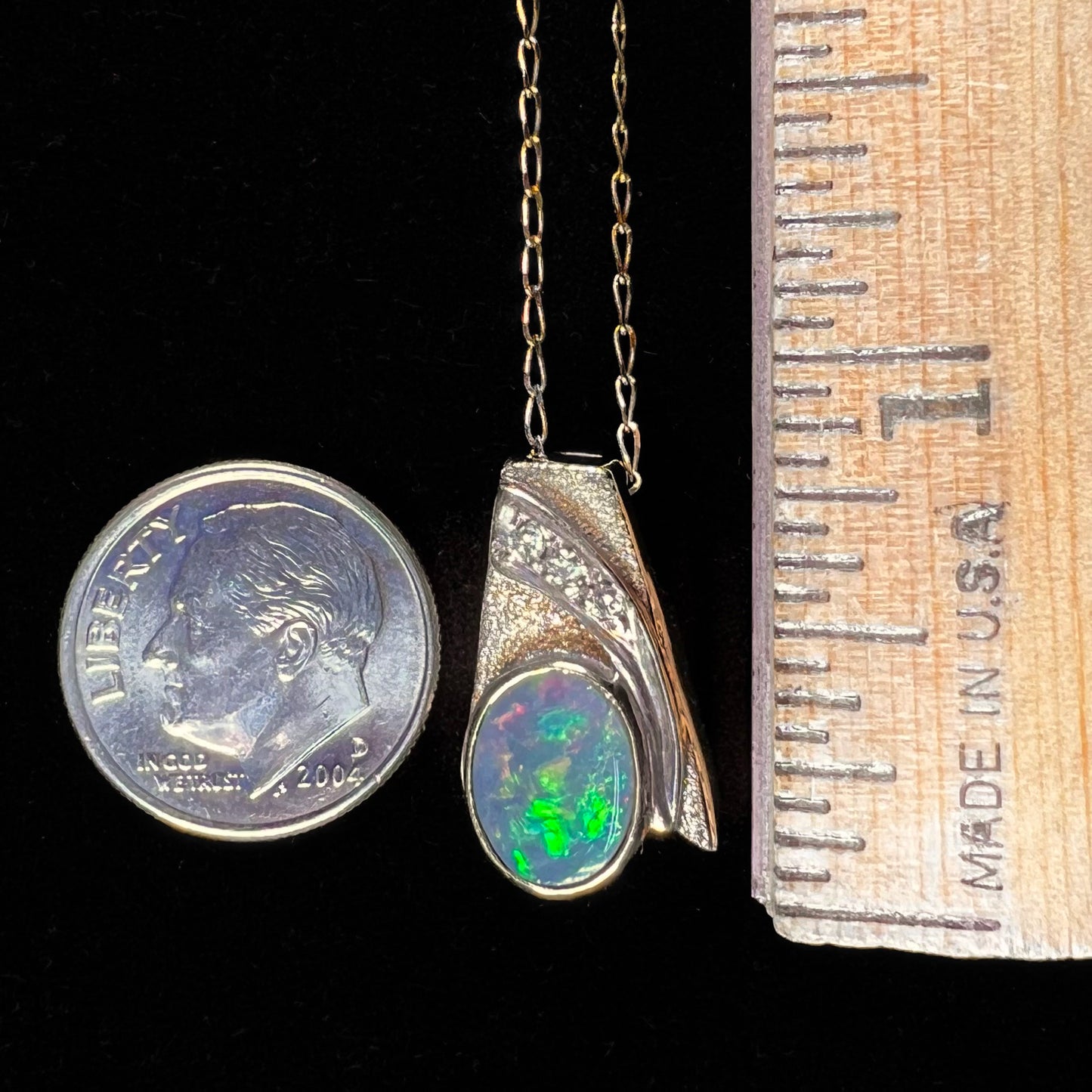 A yellow gold natural, Australian black opal necklace set with three round diamond accents.
