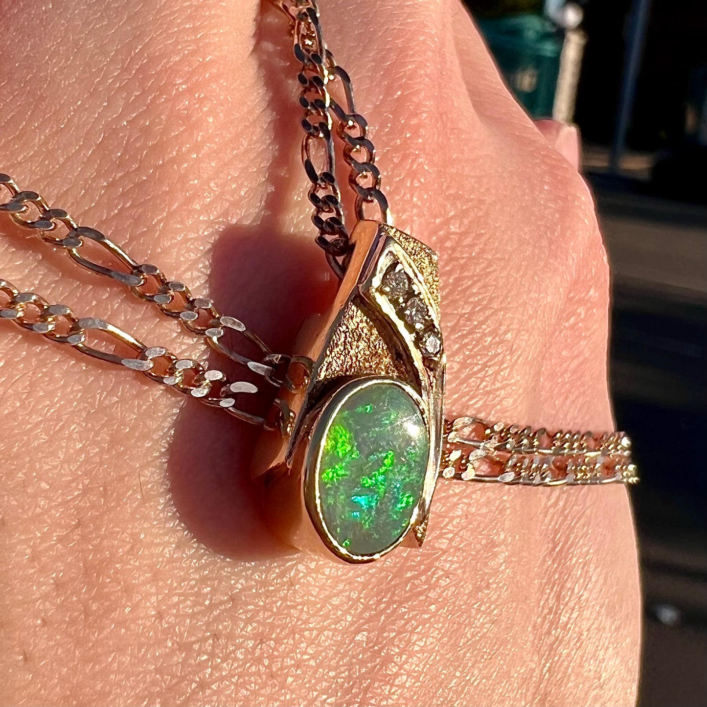A yellow gold black opal necklace set with three round diamond accents.
