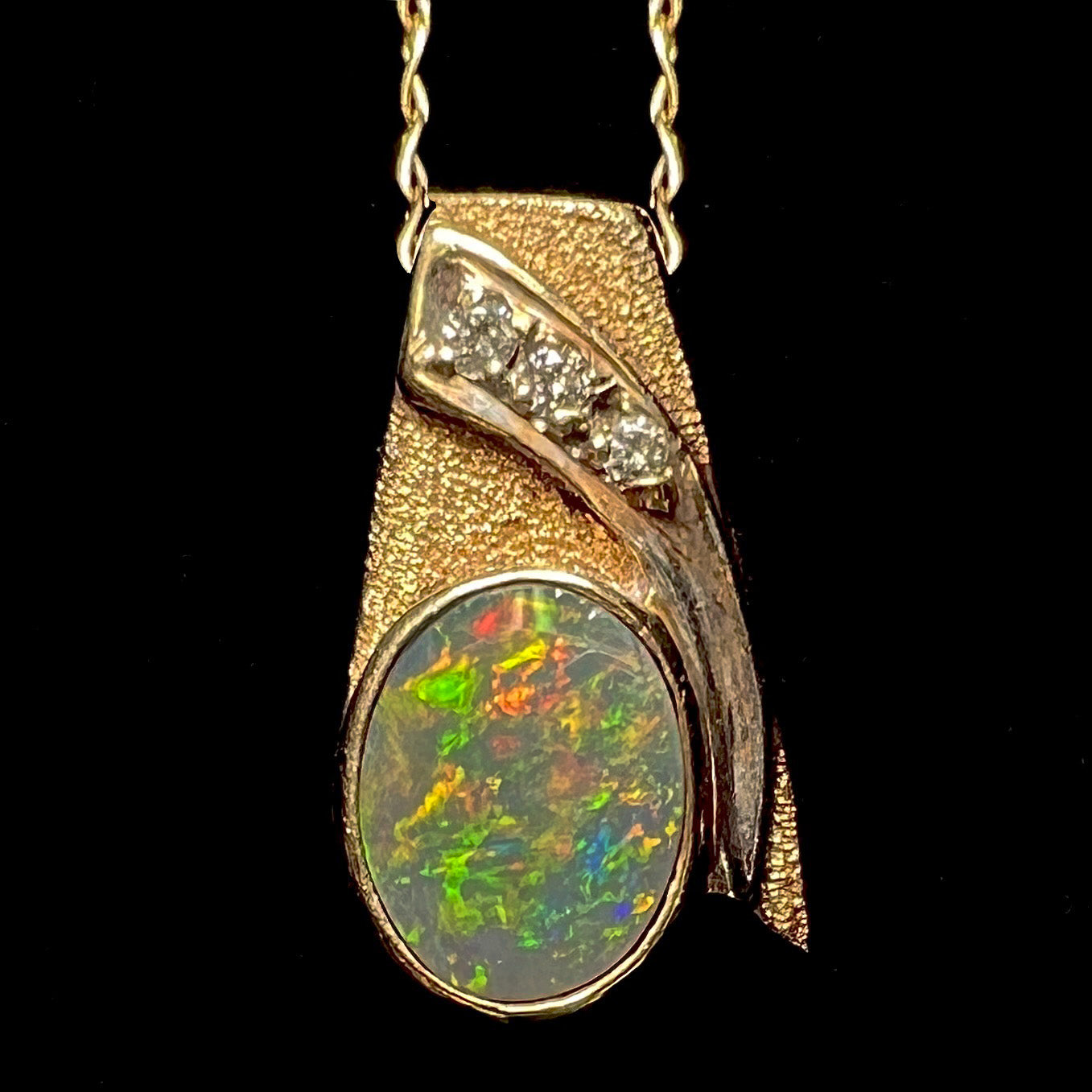 A yellow gold natural, Australian black opal necklace set with three round diamond accents.