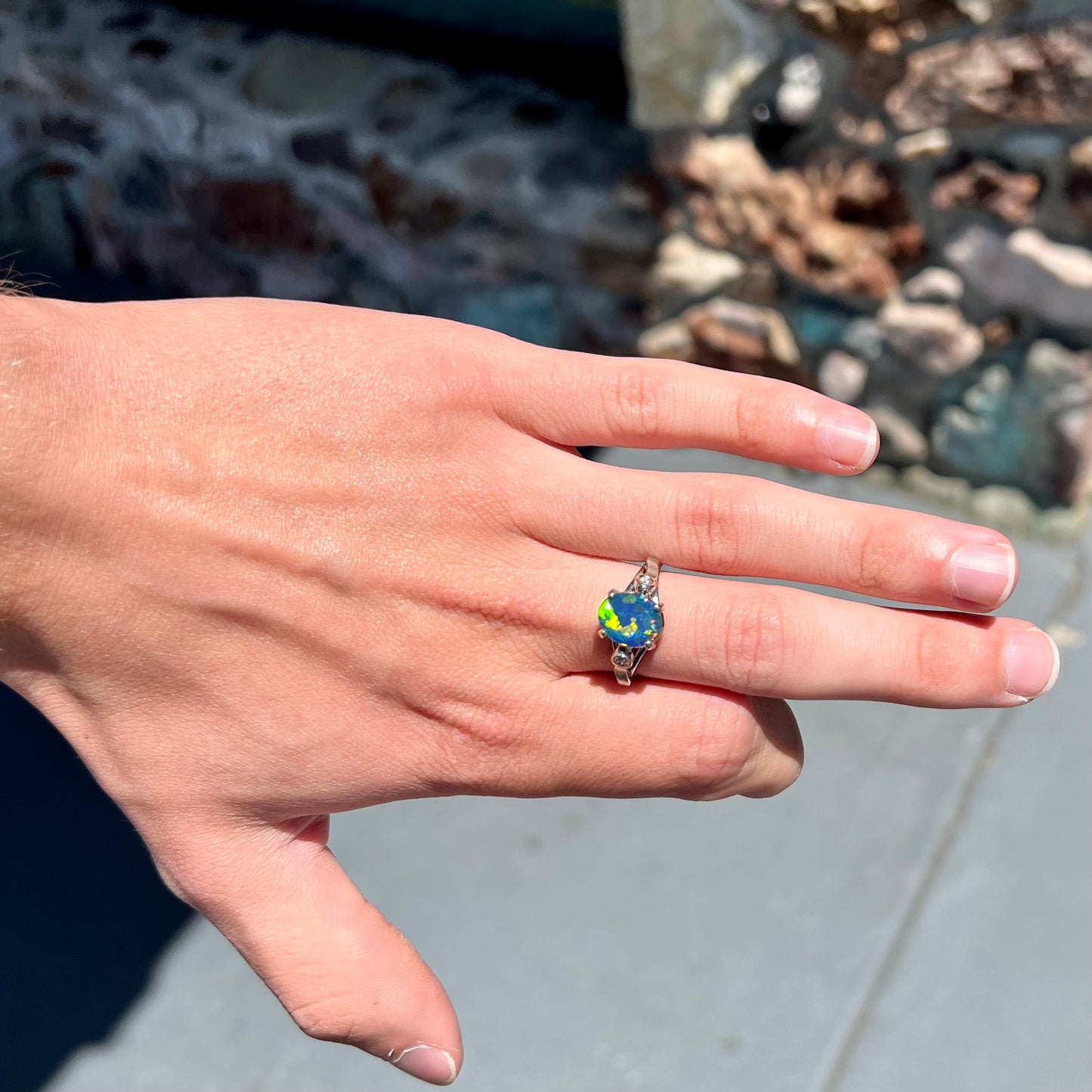 A white gold, oval cabochon cut black opal doublet ring set with two round diamond accent stones.