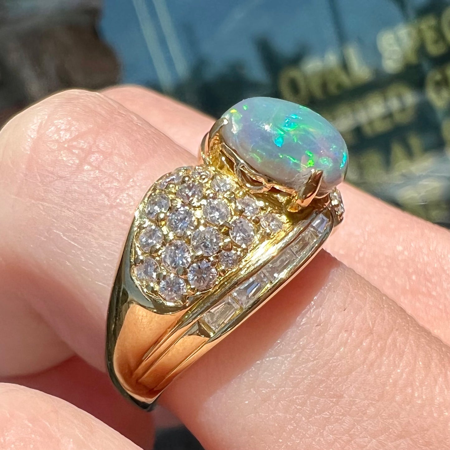 An 18kt yellow gold oval cabochon cut Lightning Ridge black opal ring. The shank is set with round and baguette cut diamonds.