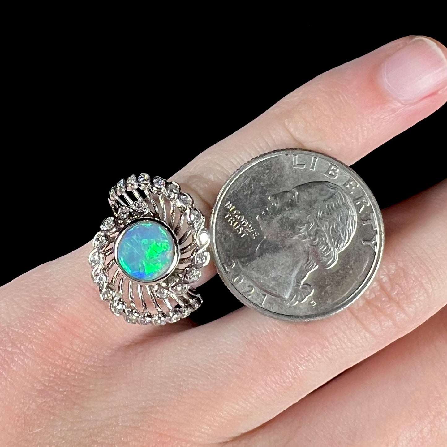 A white gold ring featuring a round cabochon cut black opal set in a swirl of round cut diamonds.