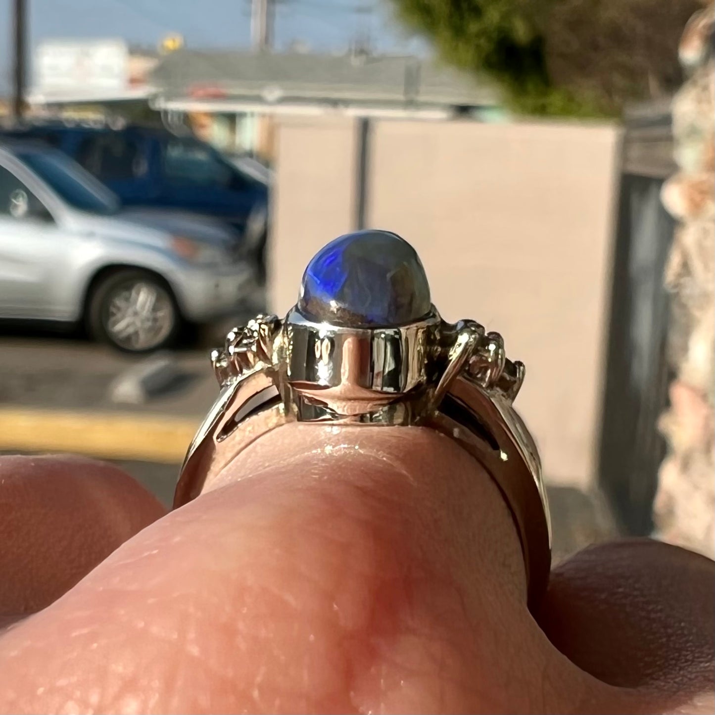 A white gold ring set with a Lightning Ridge black opal and diamond accents. The opal displays a cat's eye pattern.