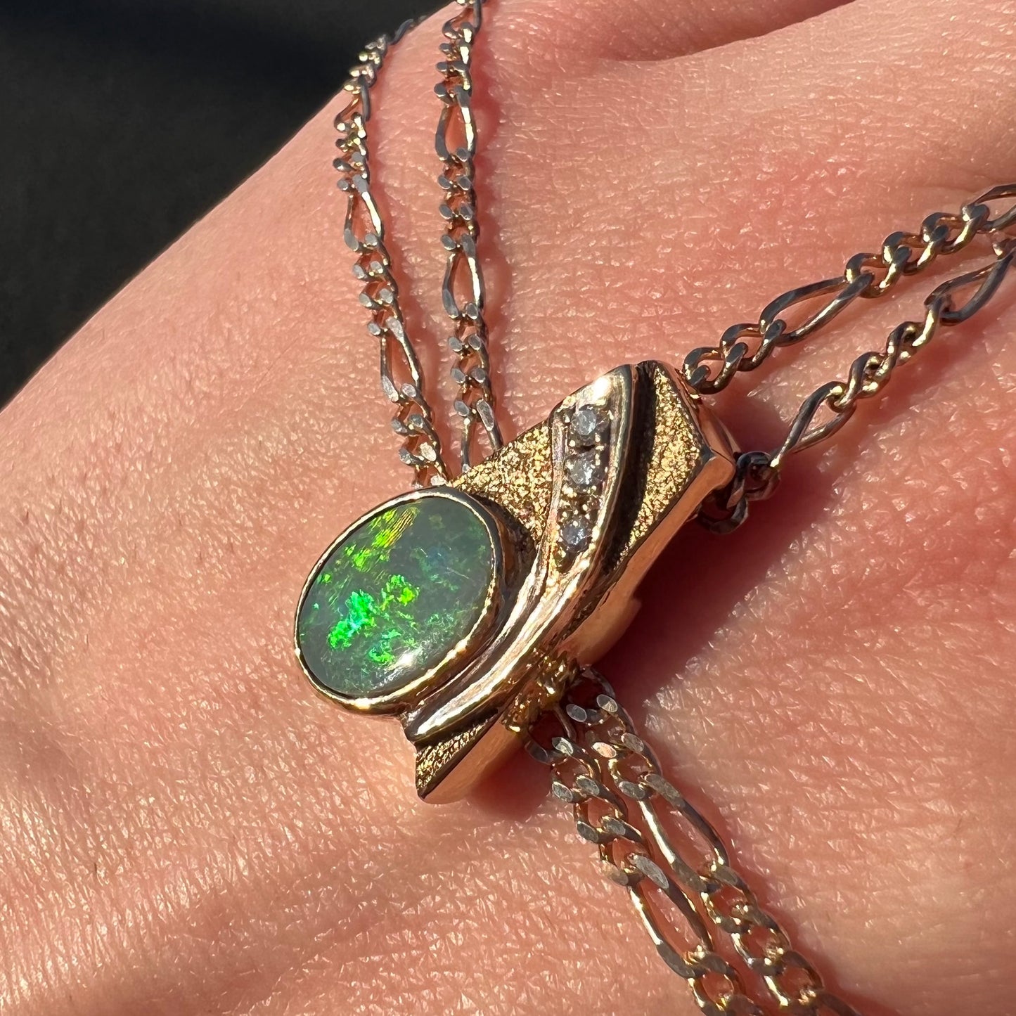 A yellow gold black opal necklace set with three round diamond accents.