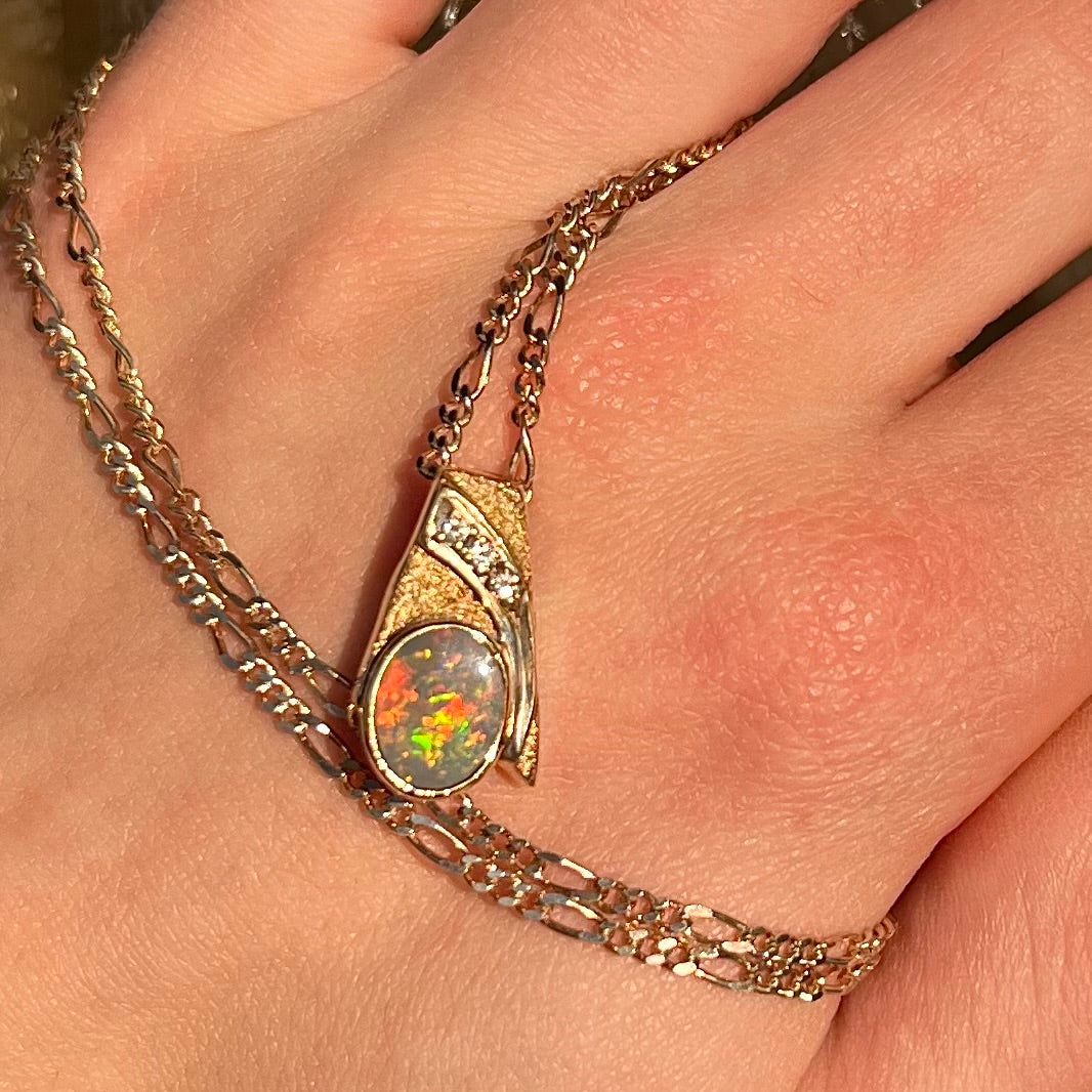 A yellow gold black opal necklace set with three round diamond accents.