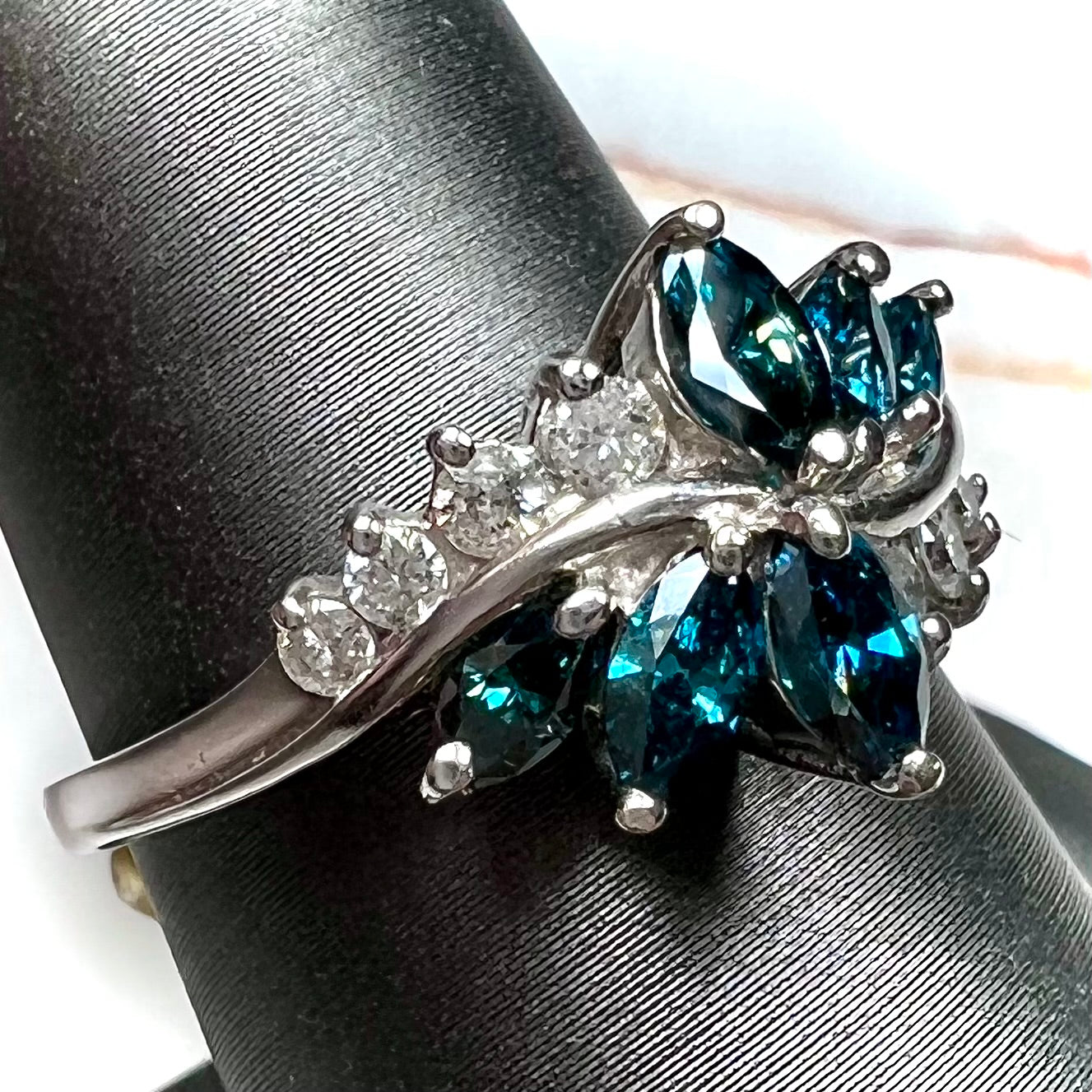 A white gold diamond cluster ring set with blue marquise cut and white round cut diamonds.