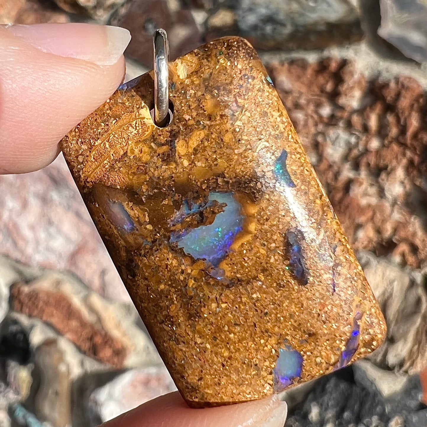 A drilled boulder opal stone with a sterling silver ring through the hole to be worn as a pendant.