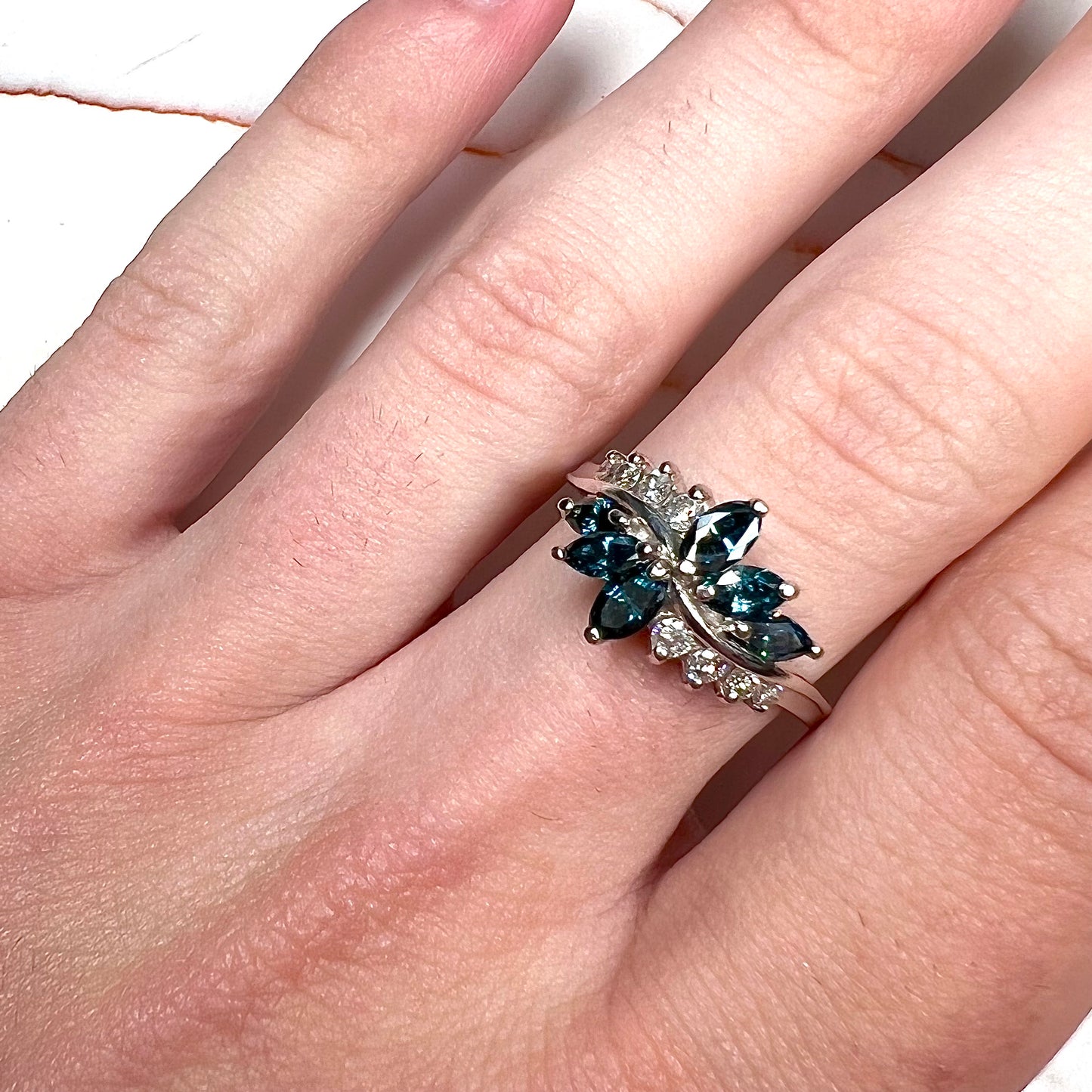 A white gold diamond cluster ring set with blue marquise cut and white round cut diamonds.