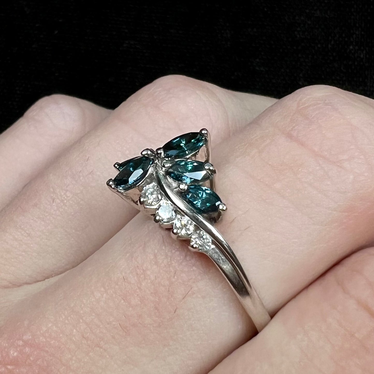 A white gold diamond cluster ring set with blue marquise cut and white round cut diamonds.