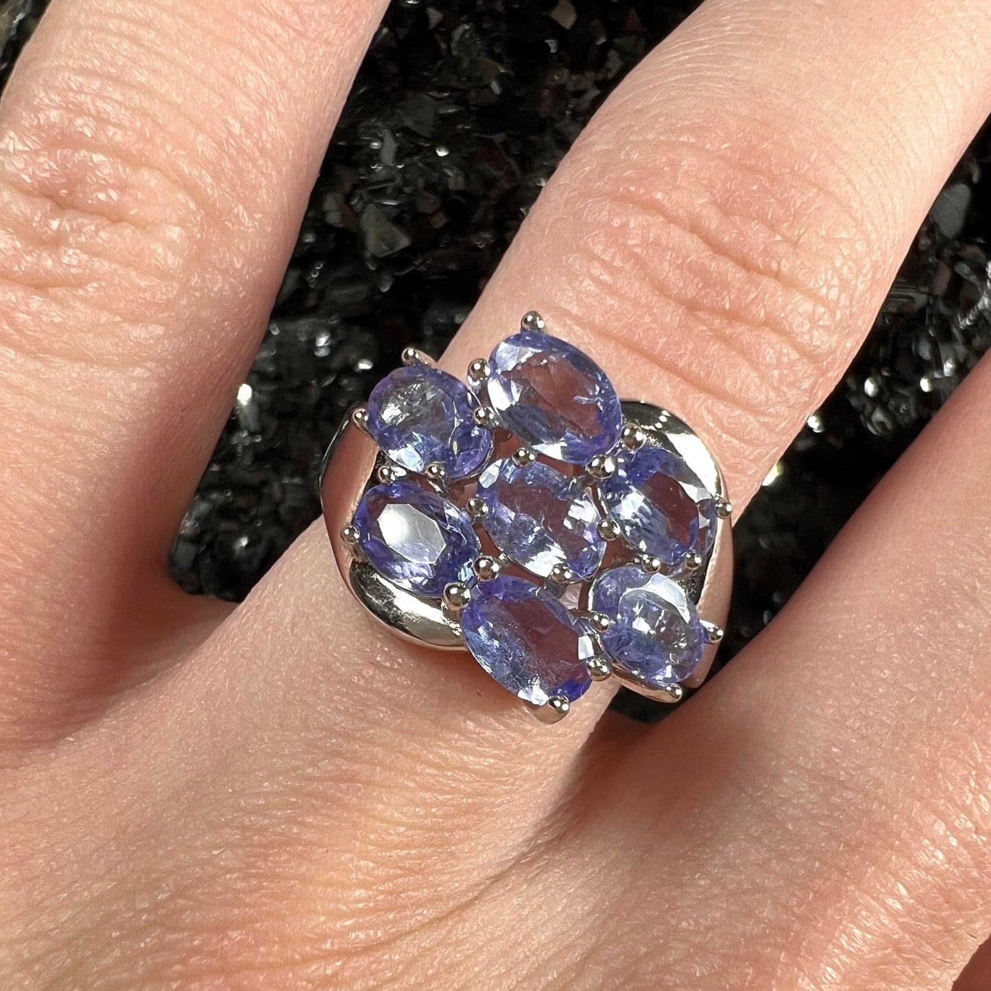 A sterling silver cluster ring prong set with seven faceted oval cut blue tanzanite stones.