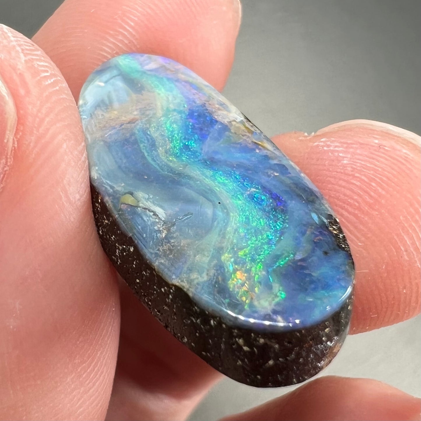 A loose, oval cabochon cut Quilpie boulder opal from Queensland, Australia. The stone is blue with green fire.