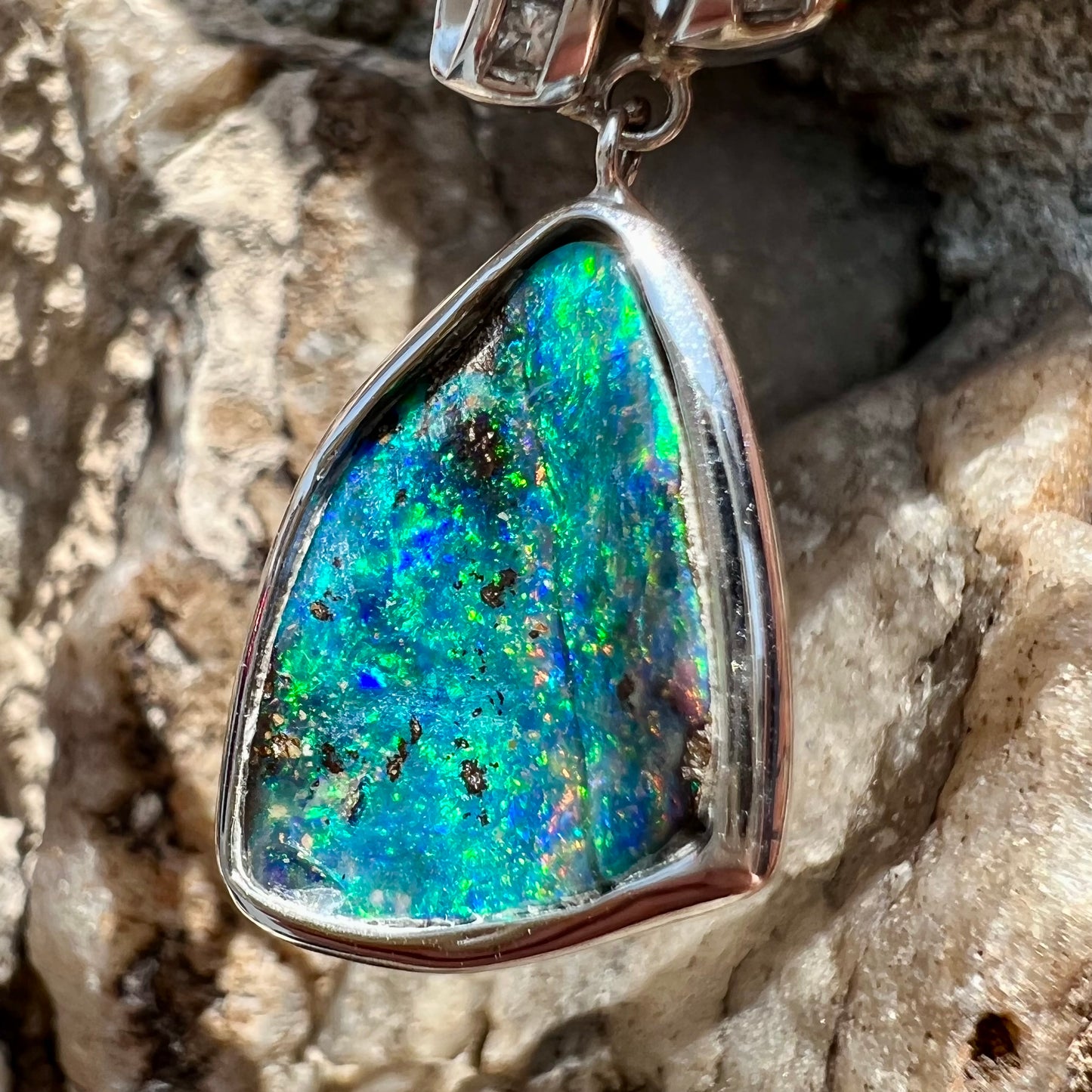 A white gold necklace set with diamonds and a dangling, bezel set boulder opal.