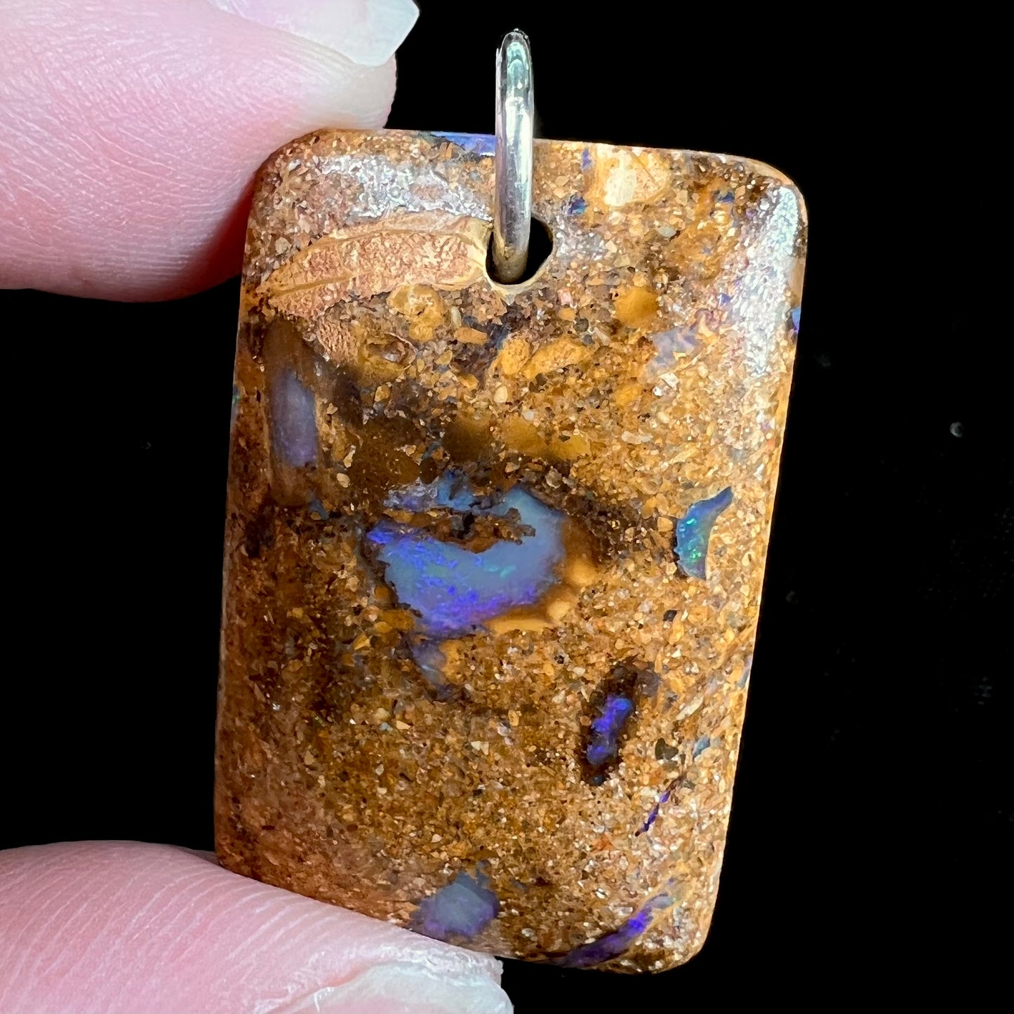 A drilled boulder opal stone with a sterling silver ring through the hole to be worn as a pendant.