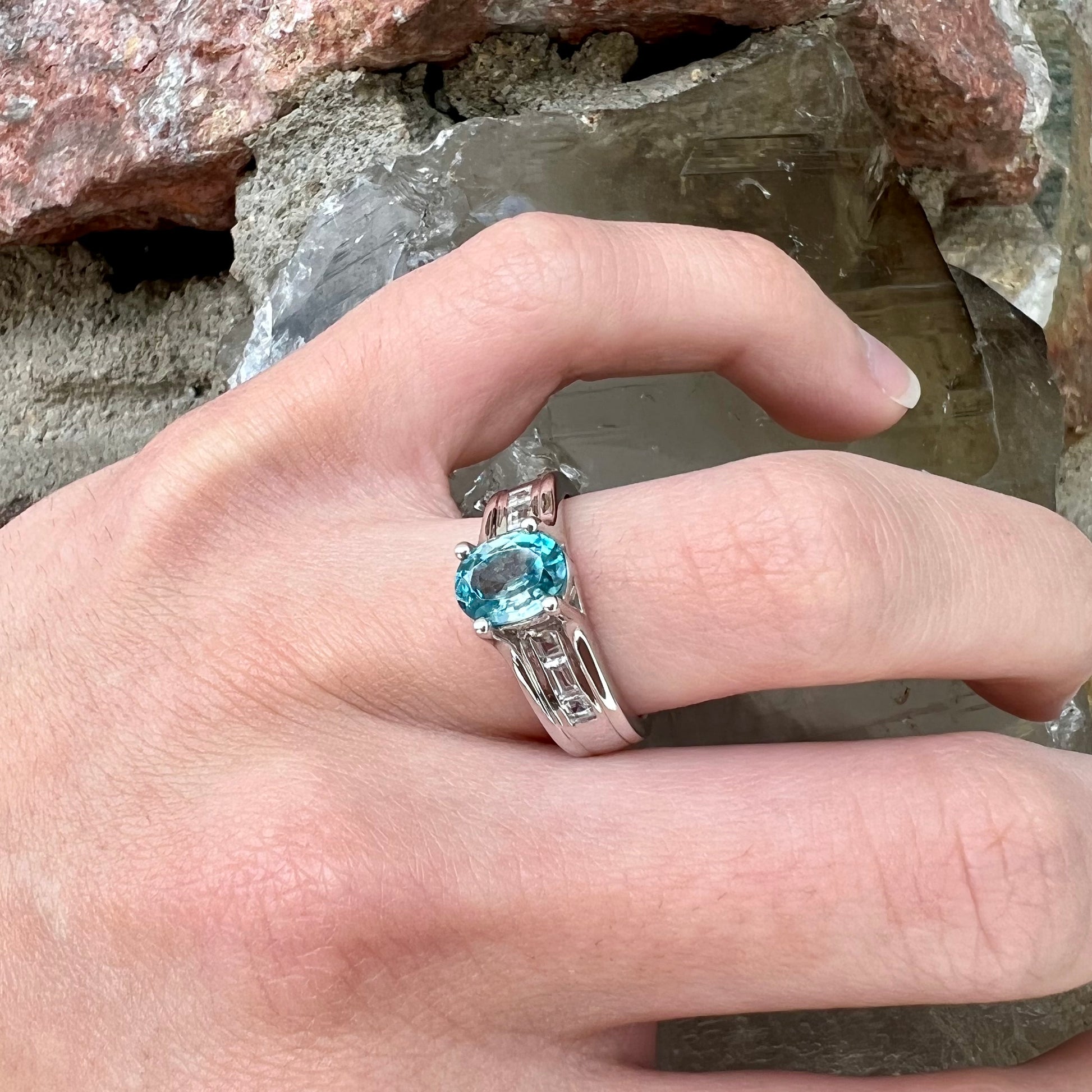 A sterling silver ring set with an oval cut blue zircon center stone and channel set white zircon accents.