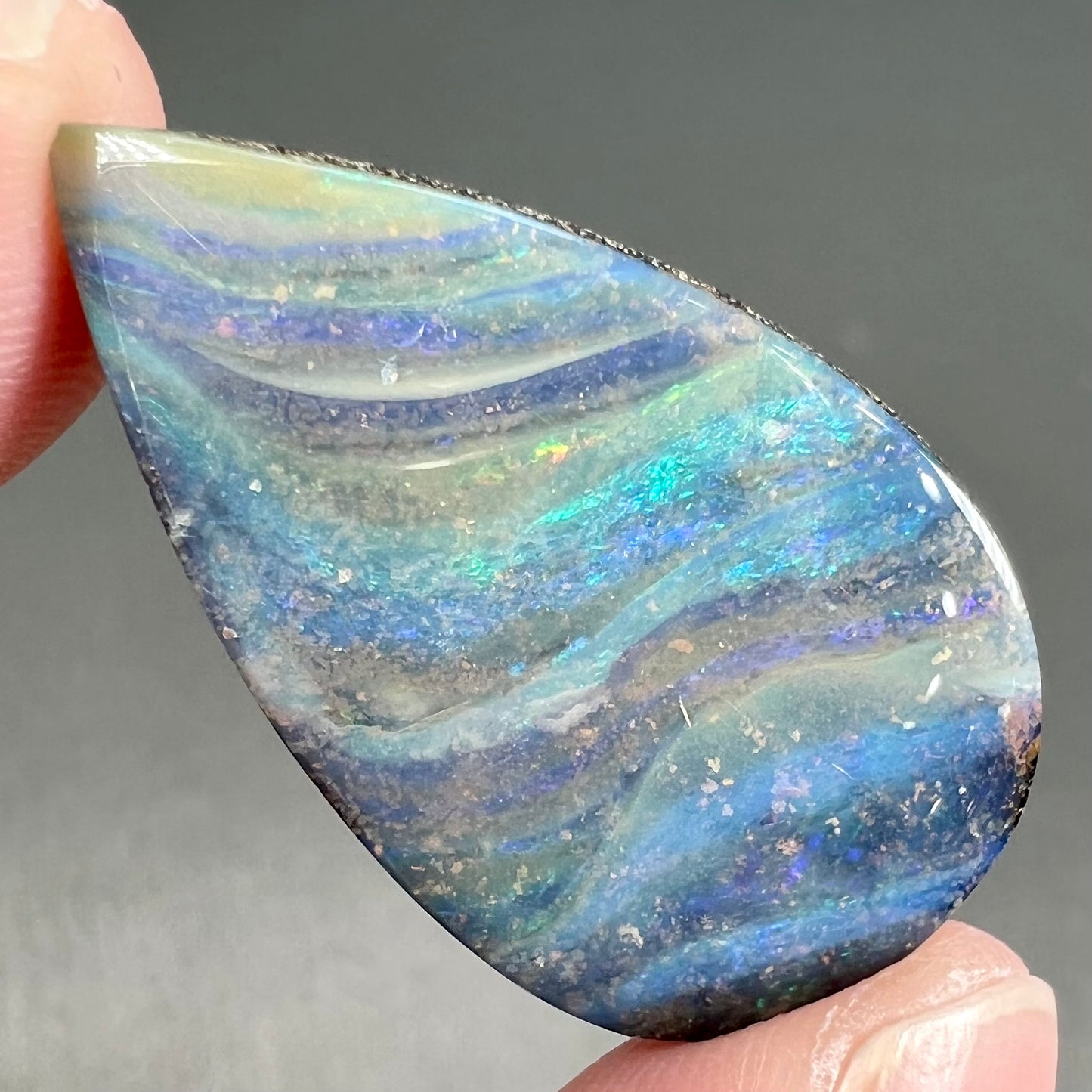 A loose, pear shaped boulder opal stone from Quilpie, Australia. The stone is predominantly blue, green, and purple with red and orange undertones.
