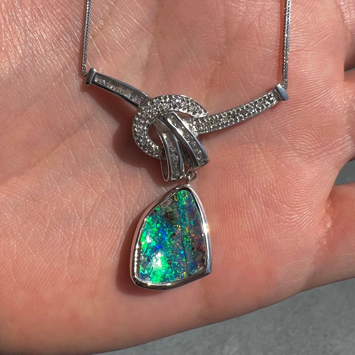 A white gold necklace set with diamonds and a dangling, bezel set boulder opal.