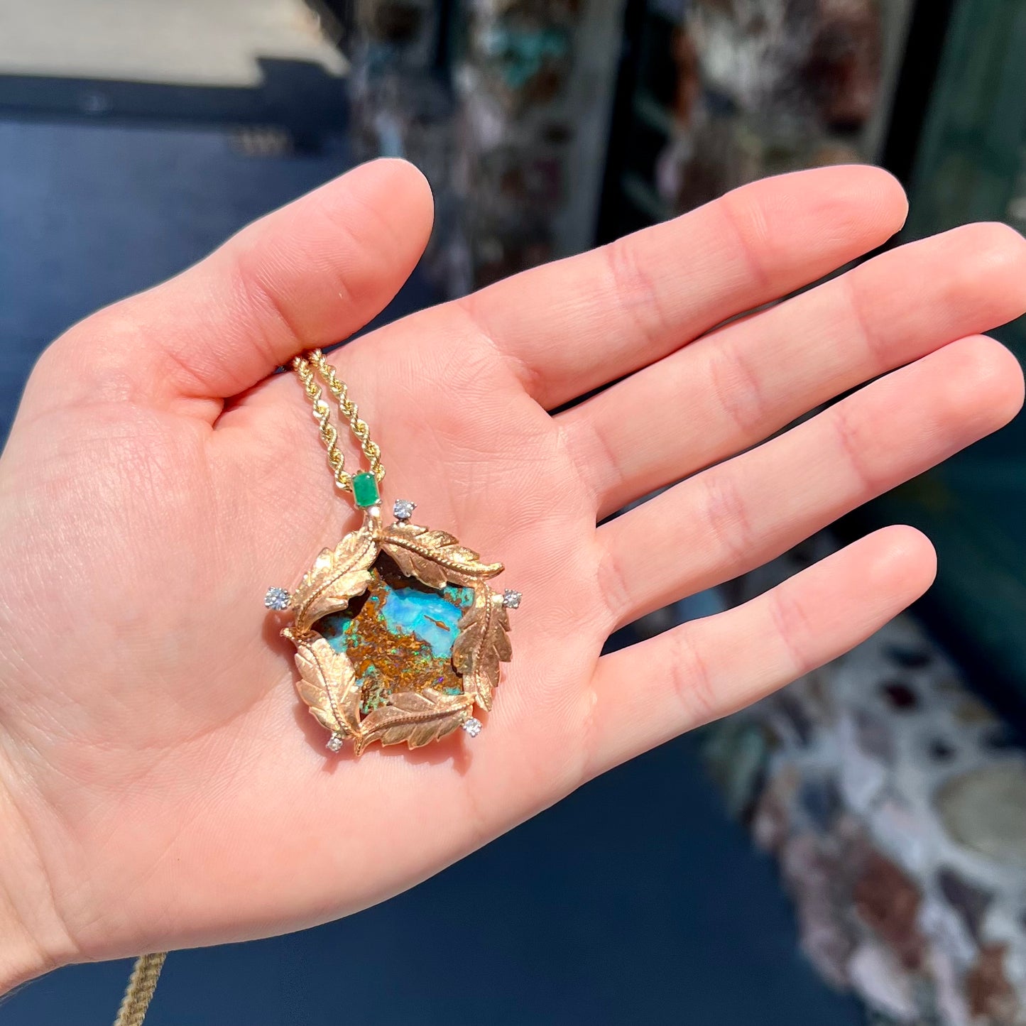A gold opalized wood, diamond, and emerald pendant. The opal is set in a wreath of gold feathers that form a star.
