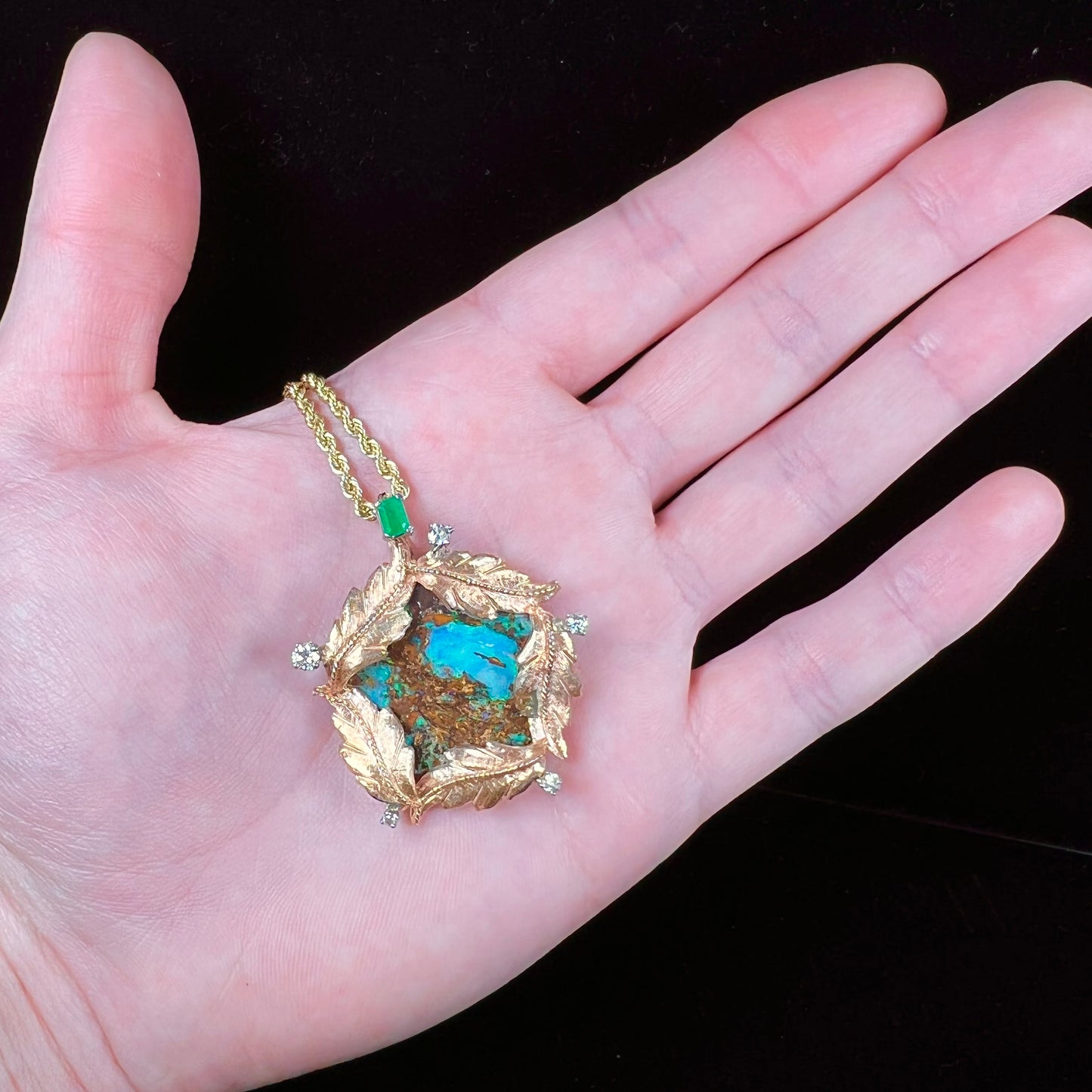 A gold opalized wood, diamond, and emerald pendant. The opal is set in a wreath of gold feathers that form a star.