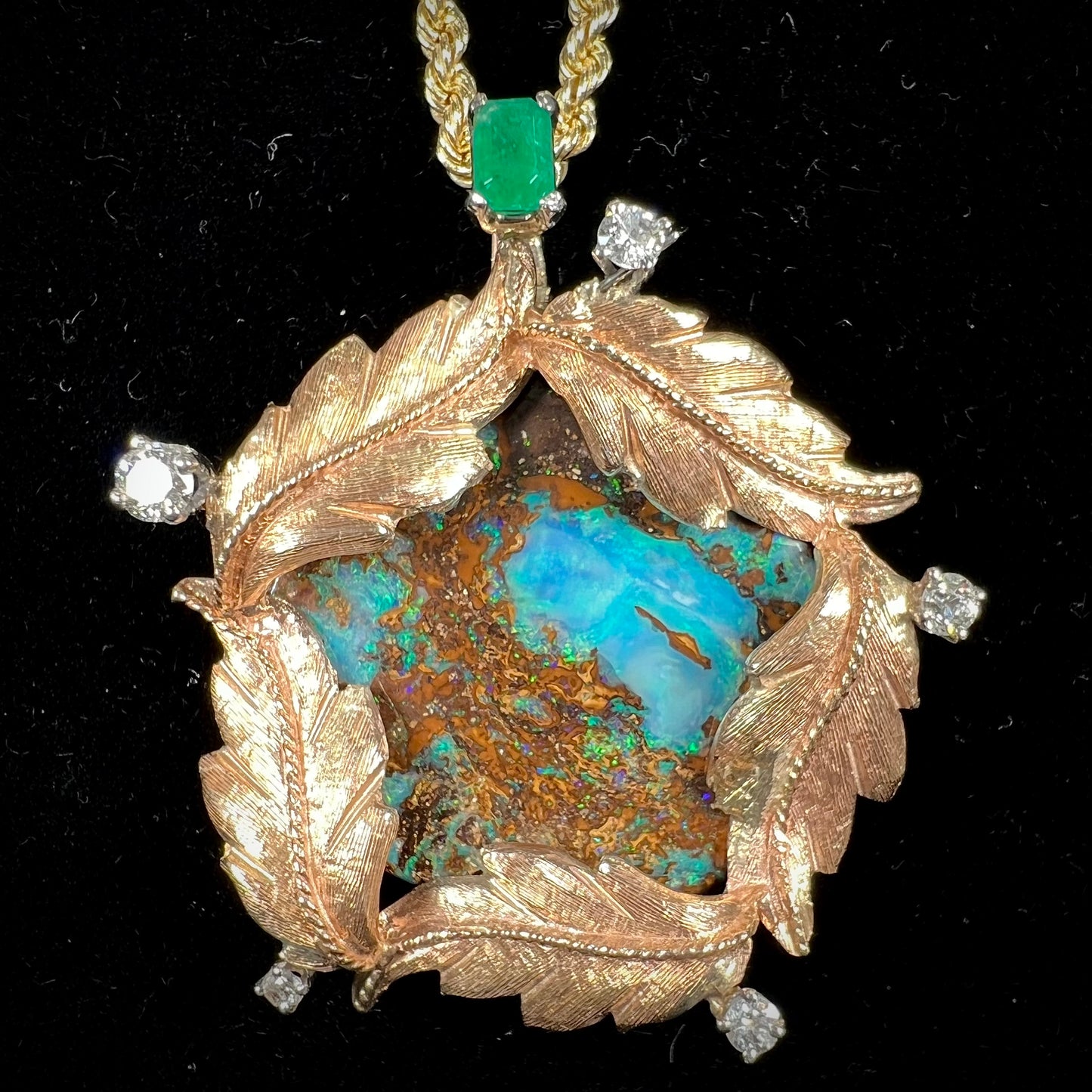 A gold opalized wood, diamond, and emerald pendant. The opal is set in a wreath of gold feathers that form a star.