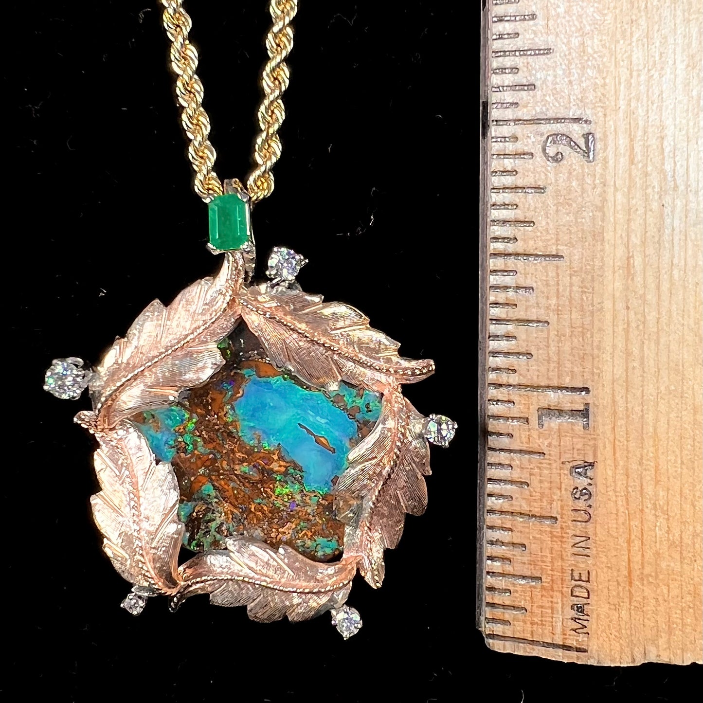 A gold opalized wood, diamond, and emerald pendant. The opal is set in a wreath of gold feathers that form a star.