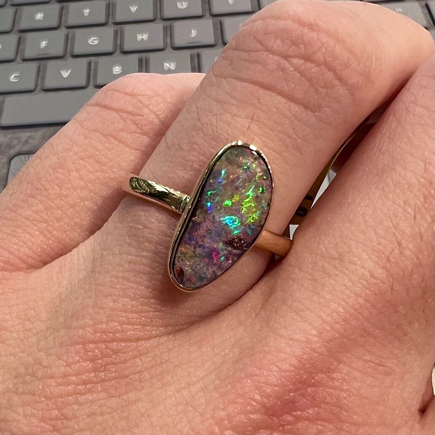 A bright, freeform cabochon cut rainbow boulder opal set in a yellow gold solitaire ring.