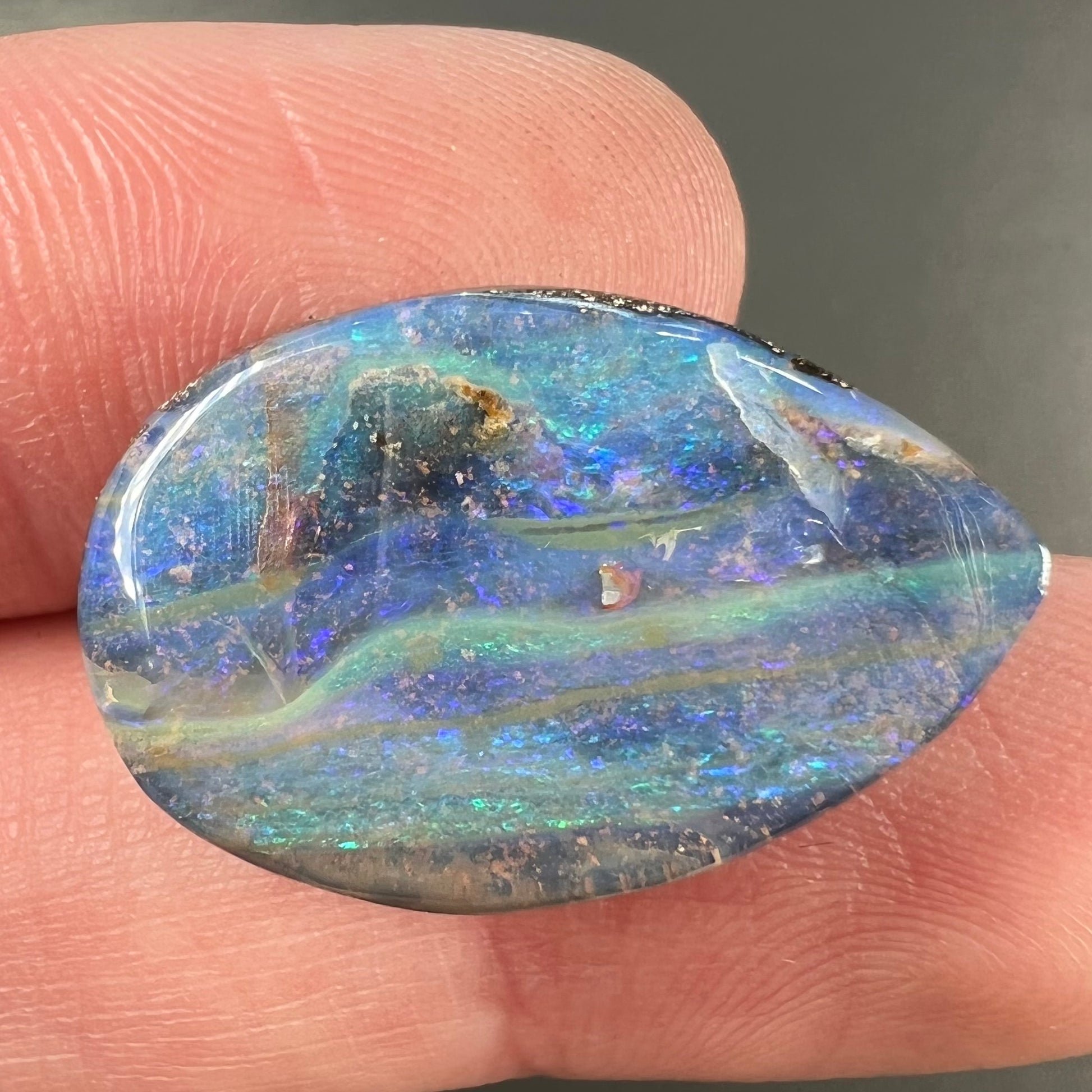 A loose, pear shaped Australian boulder opal stone.  The predominant colors are purple, green, and aqua.
