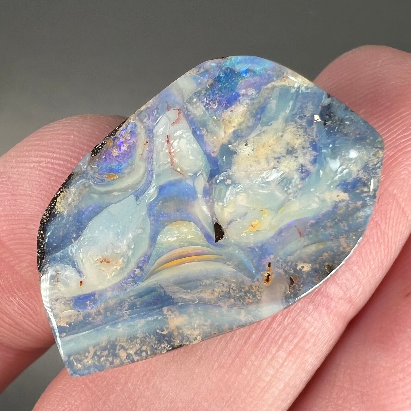 A loose, polished, freeform cut boulder opal stone from Queensland, Australia.