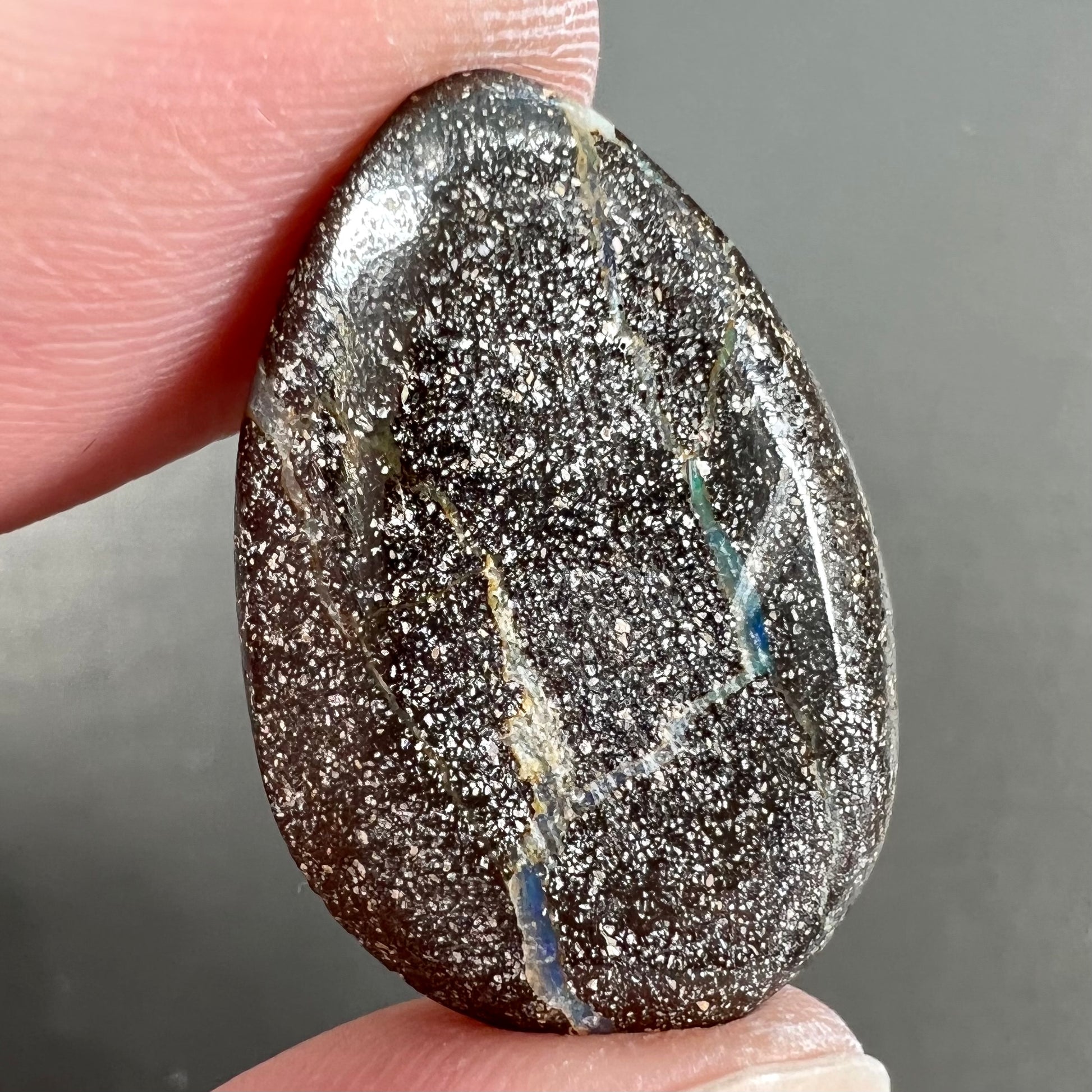 A loose, pear shaped Australian boulder opal stone.  The predominant colors are purple, green, and aqua.