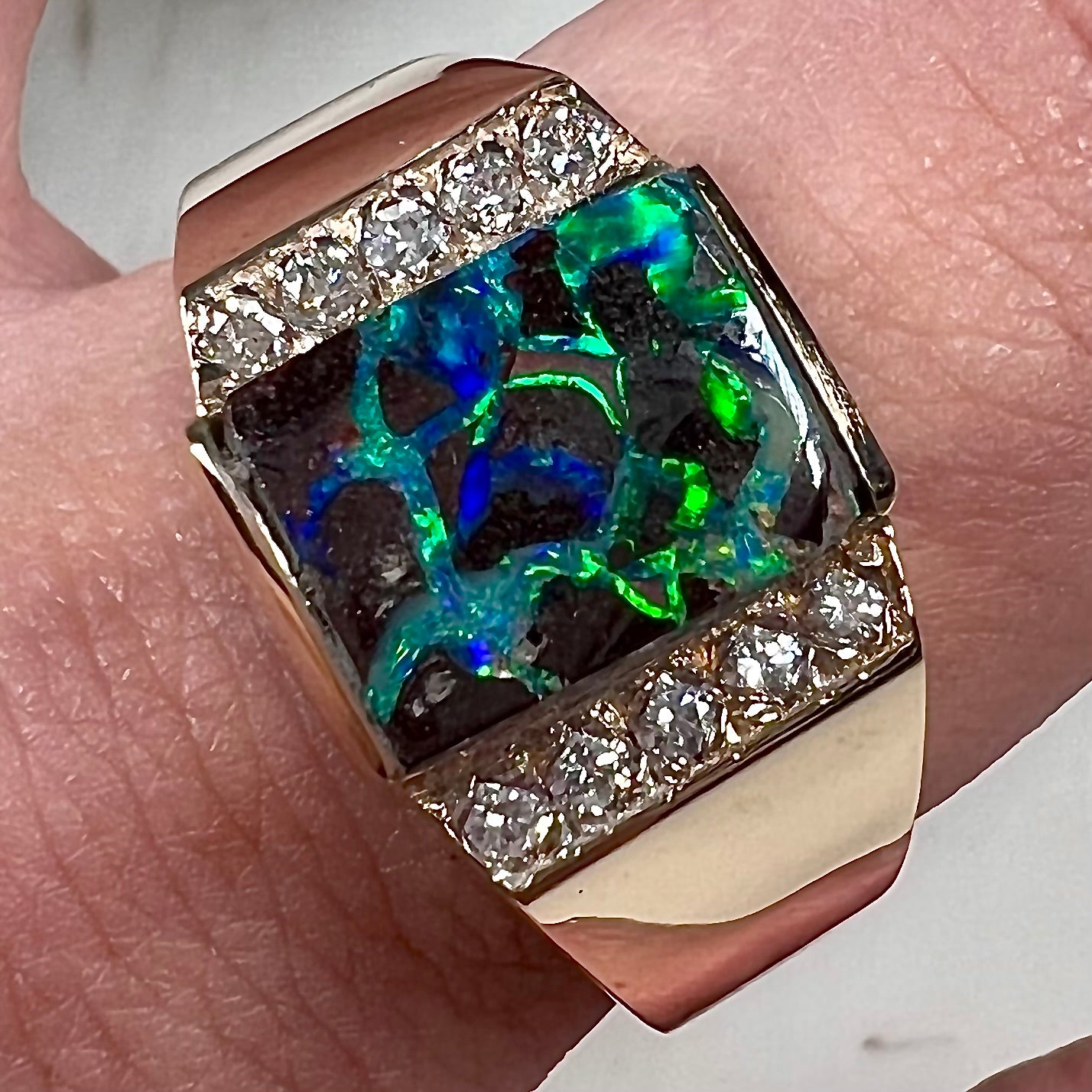 A men's gold boulder opal and diamond ring. The opal shows blue and green colors.